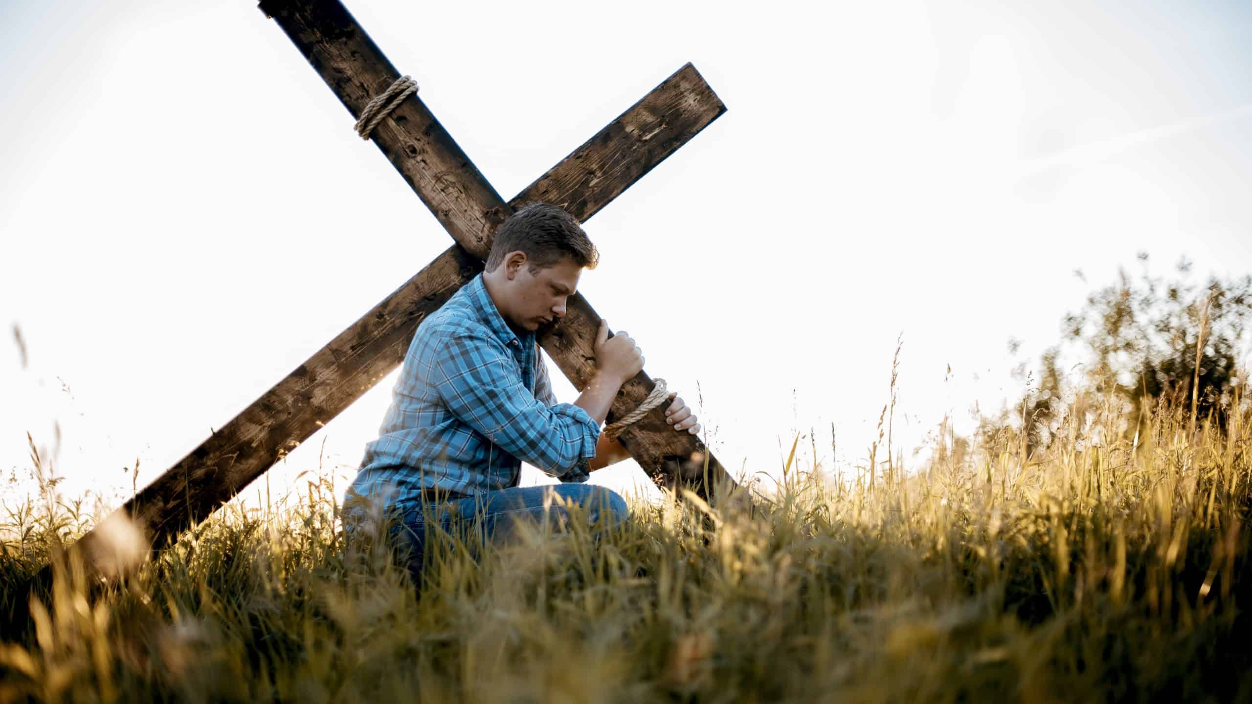 A shallow focus shot of a male carrying a handmade cross