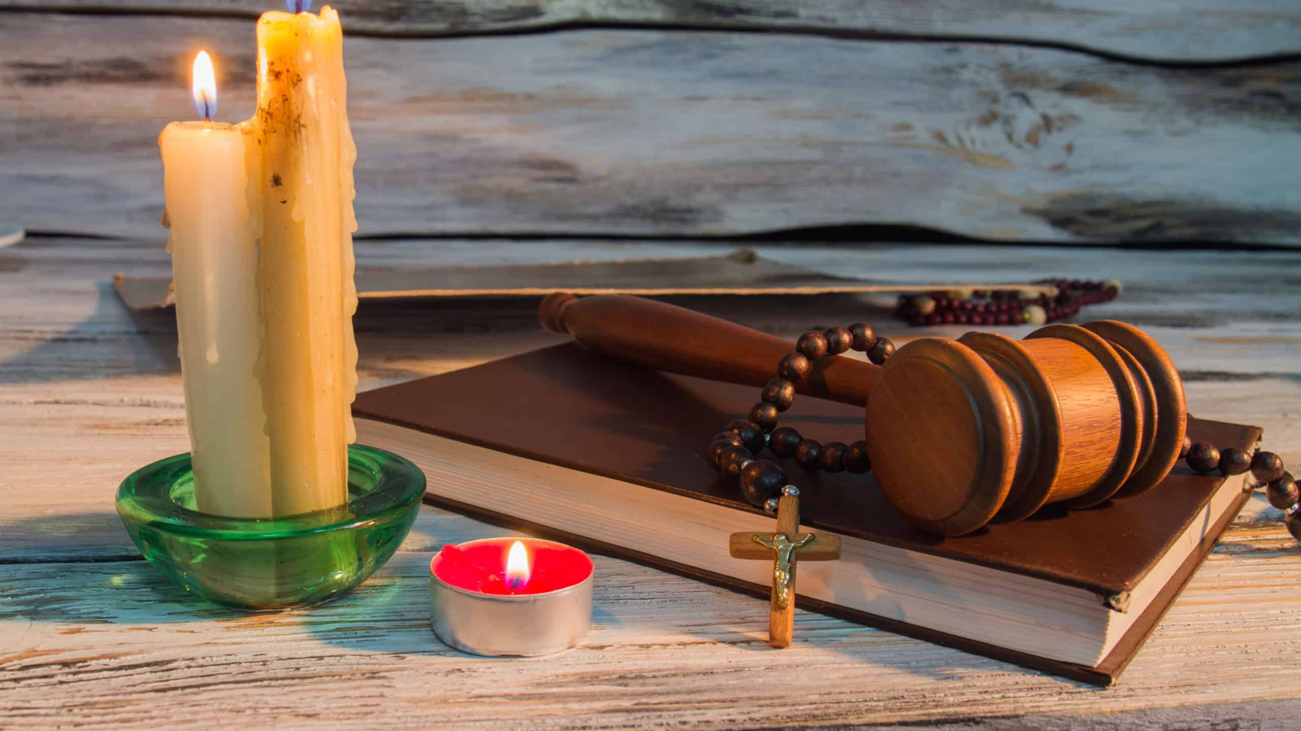Sworn testimony concept. God's justice - court hammer, holy bible, rosary with cross and burning candles on wood.