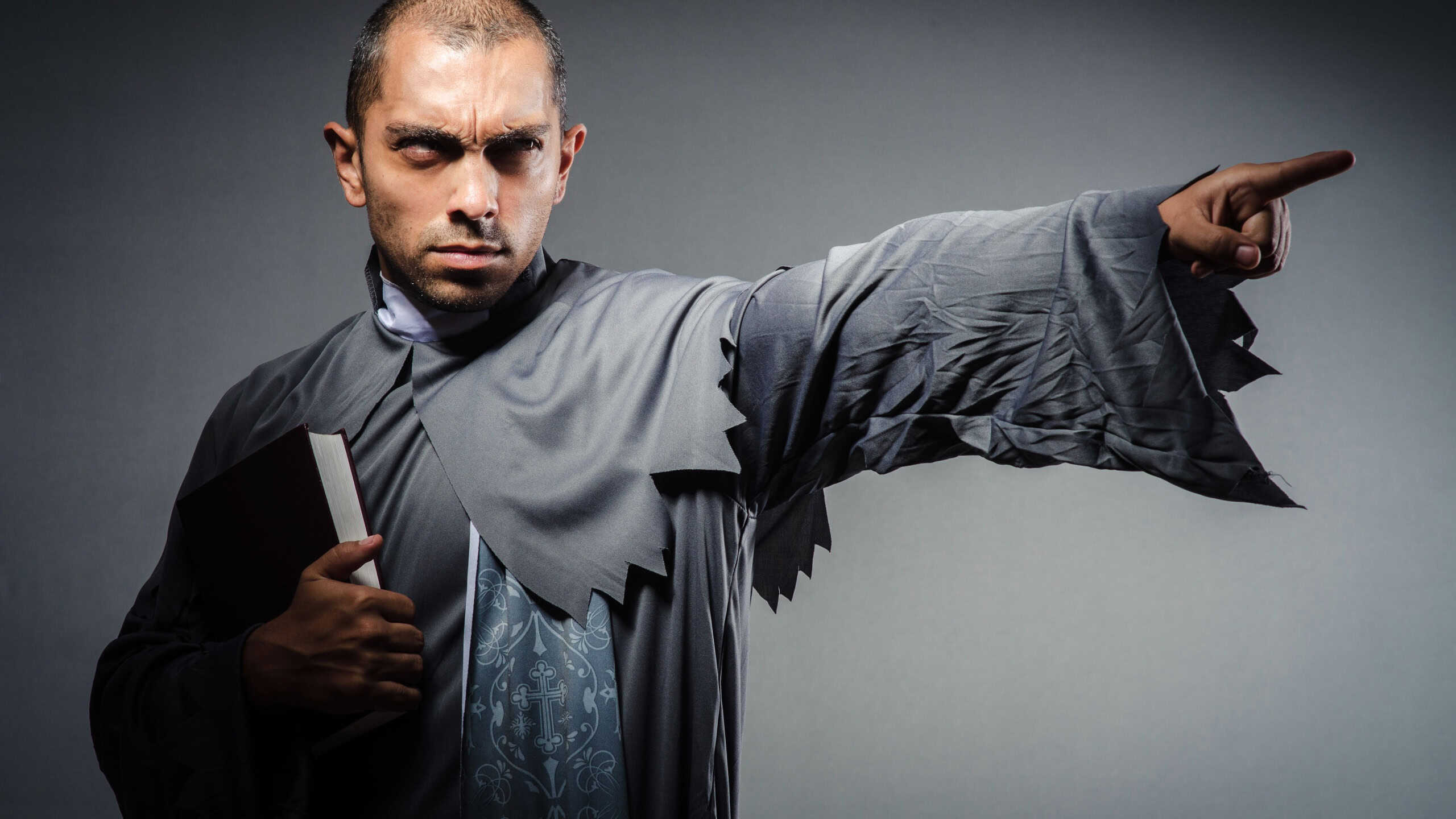Young angry priest isolated on gray background