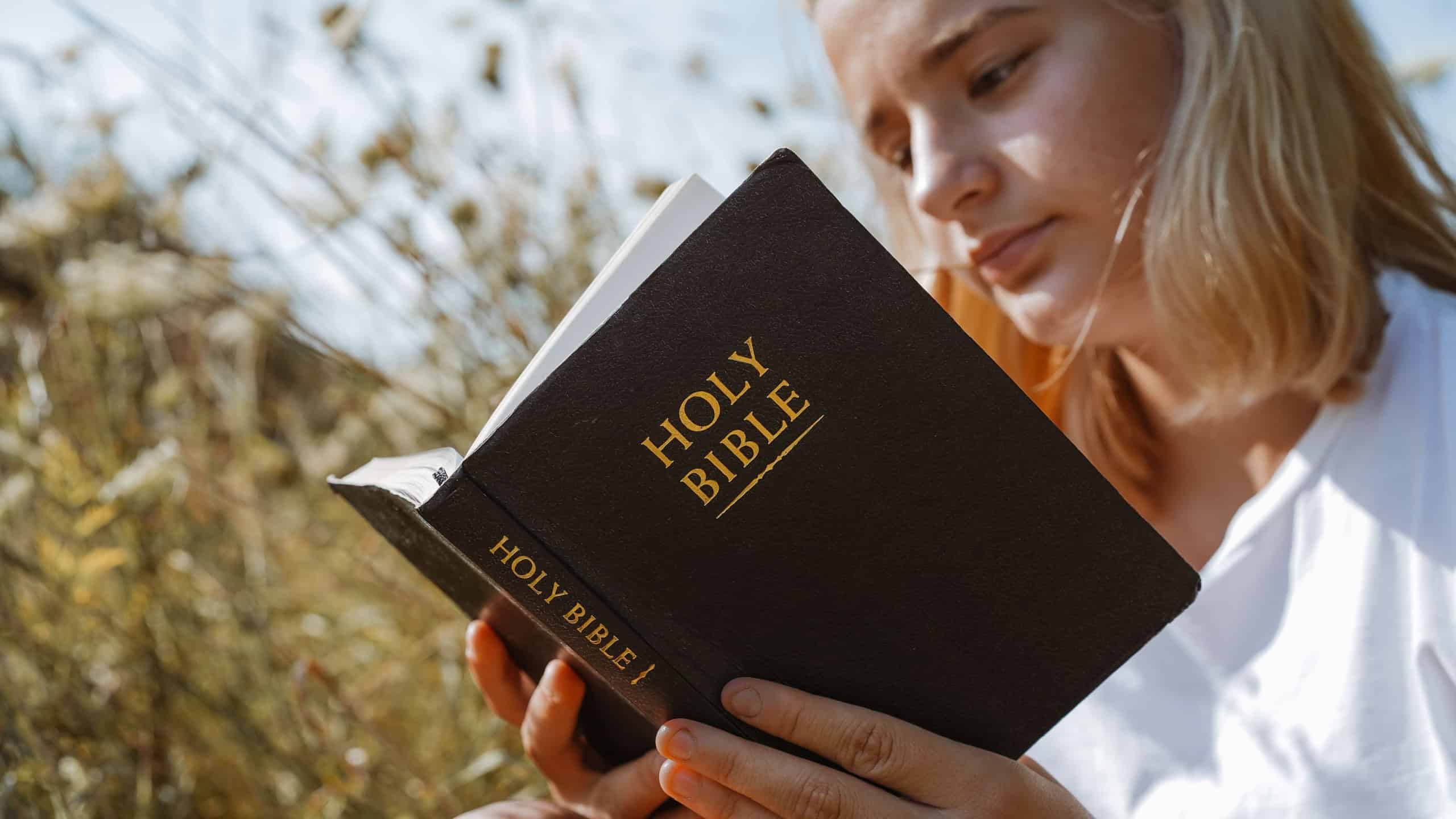 Christian teenage girl reading the Bible in the field. Faith, spirituality and religion concept. Peace, hope