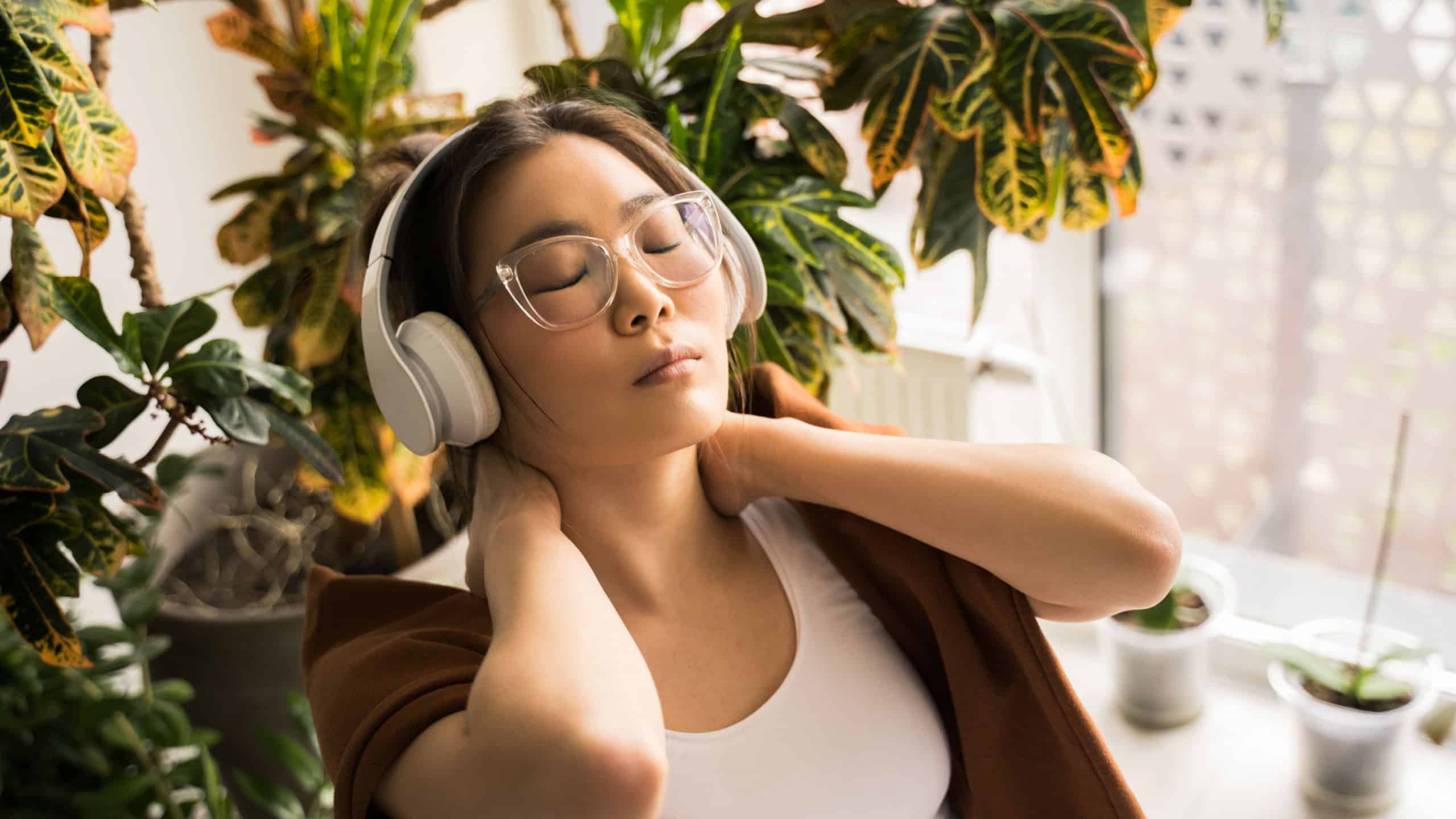 Woman resting on the armchair in wireless headphones while enjoying music