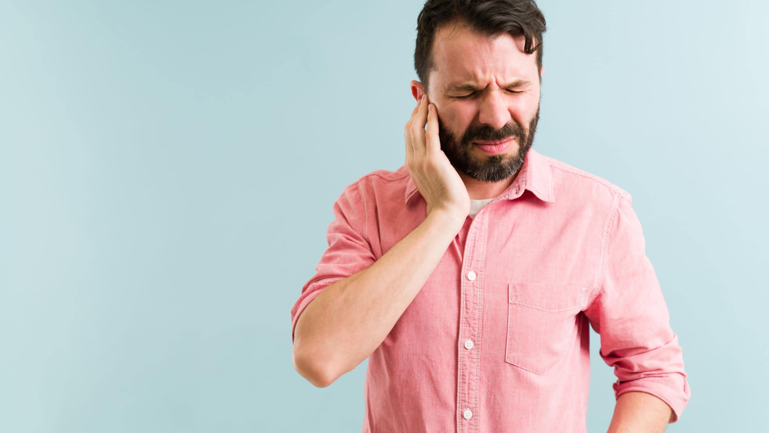 Worried man in his 30s aching and listening to a ringing in his ear. Pained man with touching his ears because of an infection