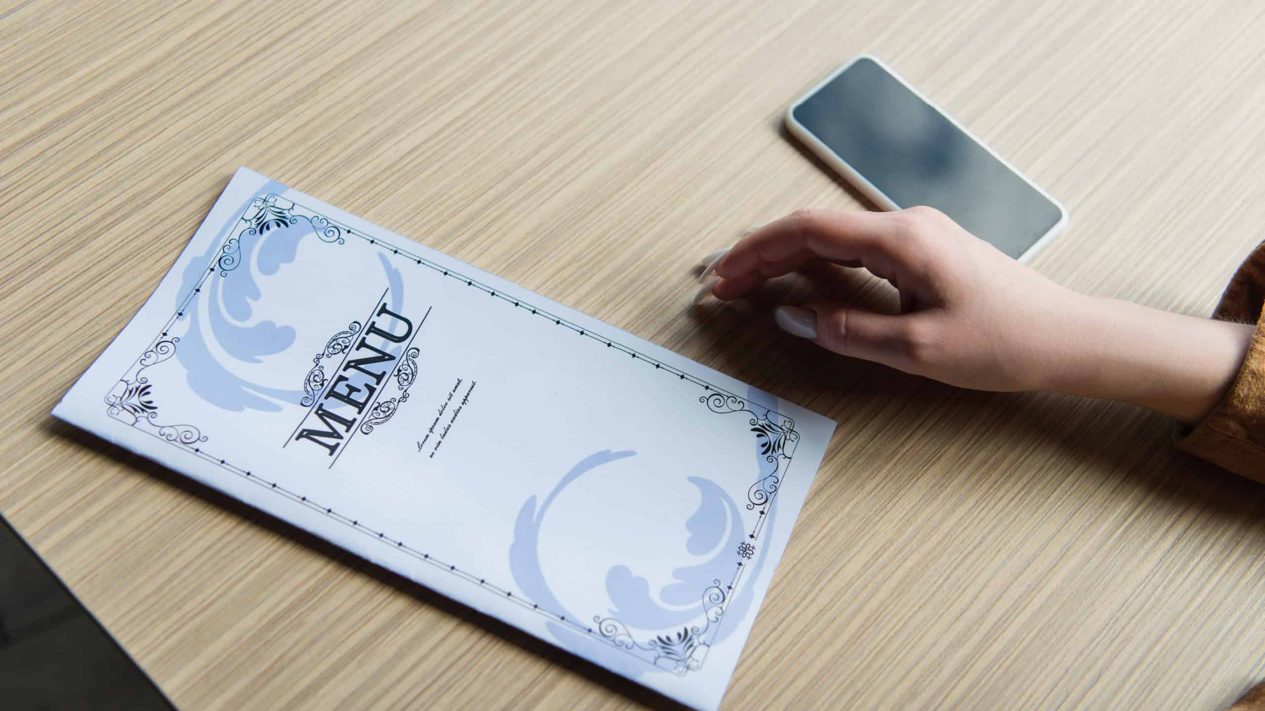 Cropped view of menu and smartphone near woman in cafe