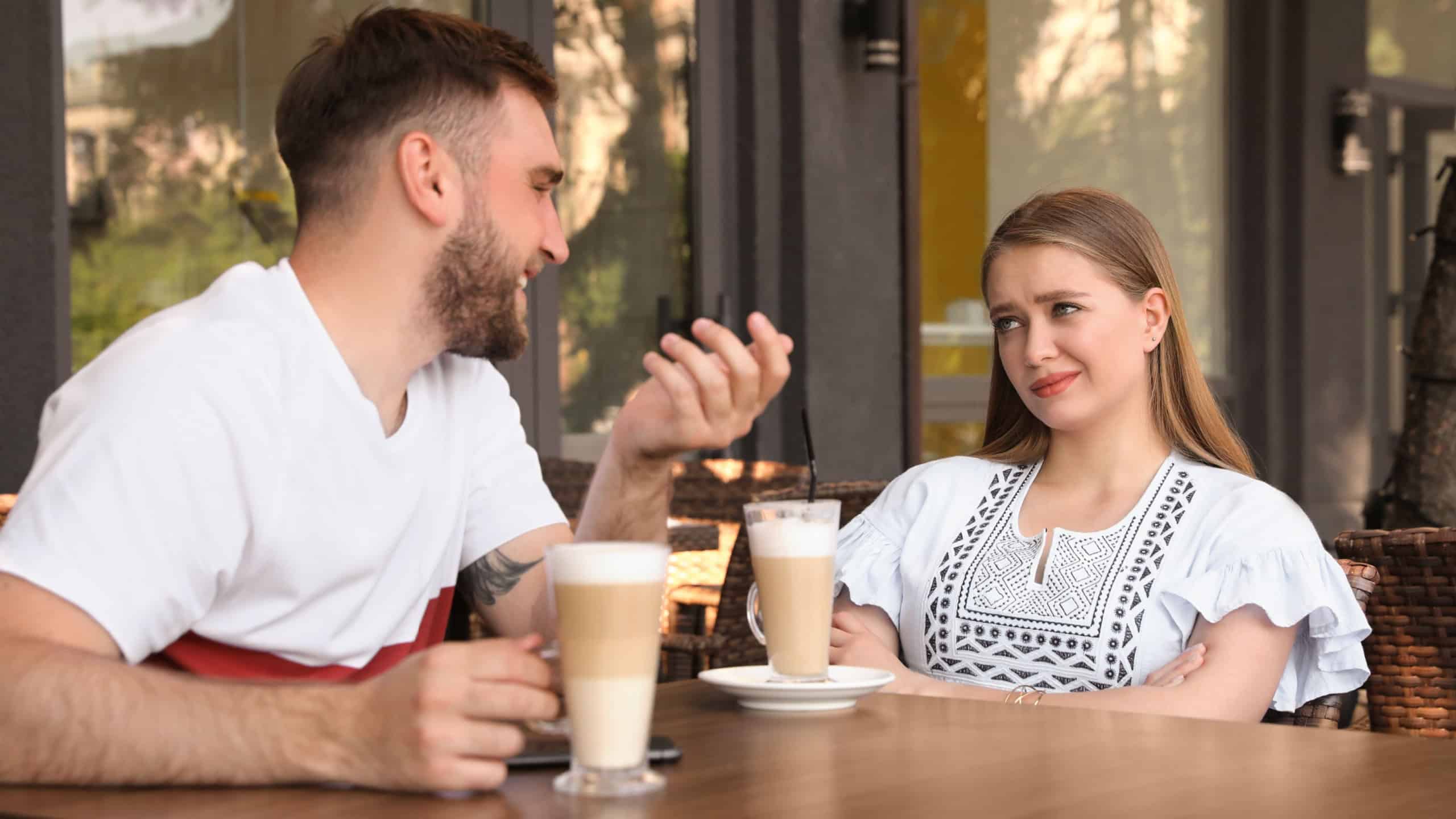 Young woman having boring date with talkative guy in outdoor cafe