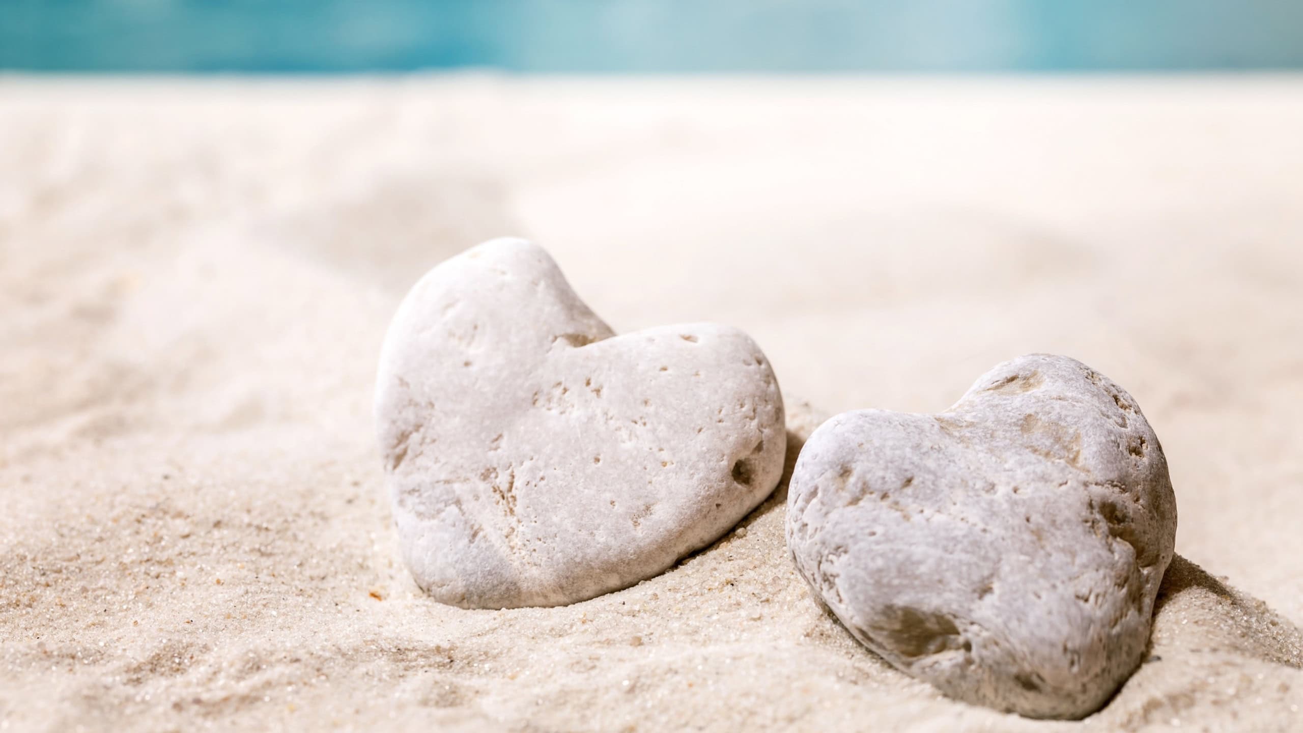 Two heart shape stones laying on summer sand sea beach with waves at background. Copy space creative layout. Love romantic vacation concept.
