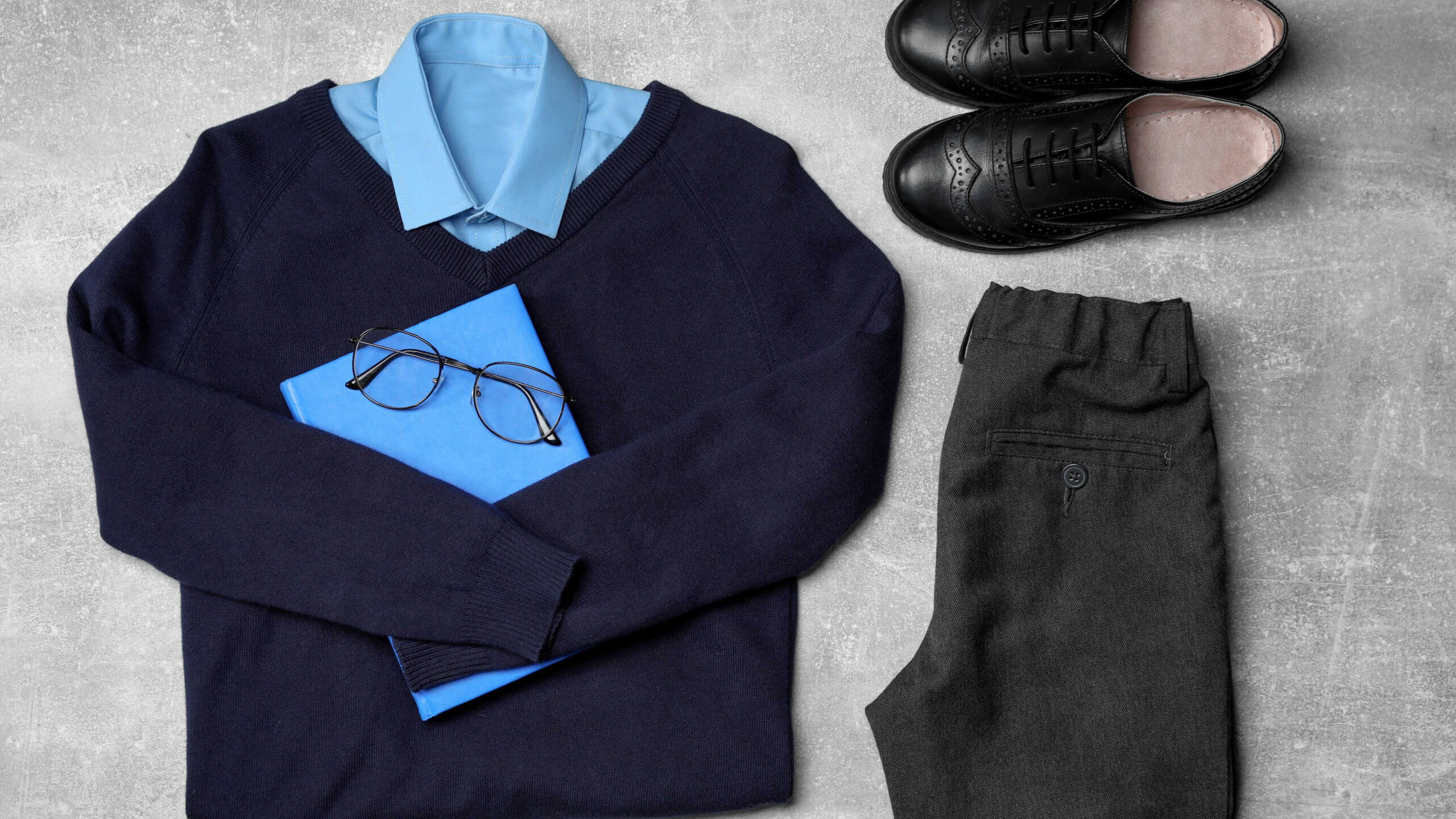 Stylish school uniform for boy, glasses and notebook on grey background, flat lay
