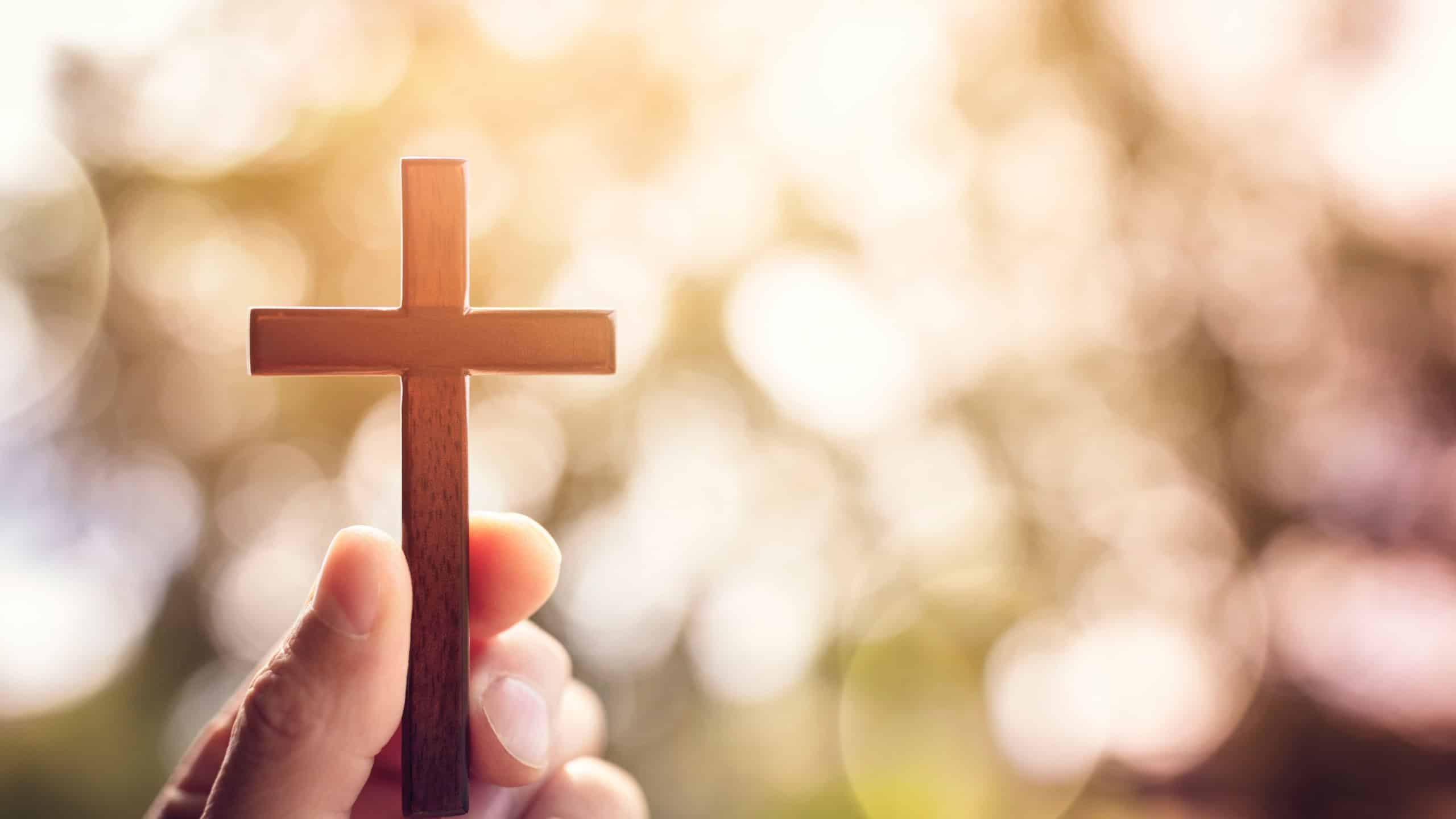 Holding religious cross crucifix outdoors with sunset background with copy space