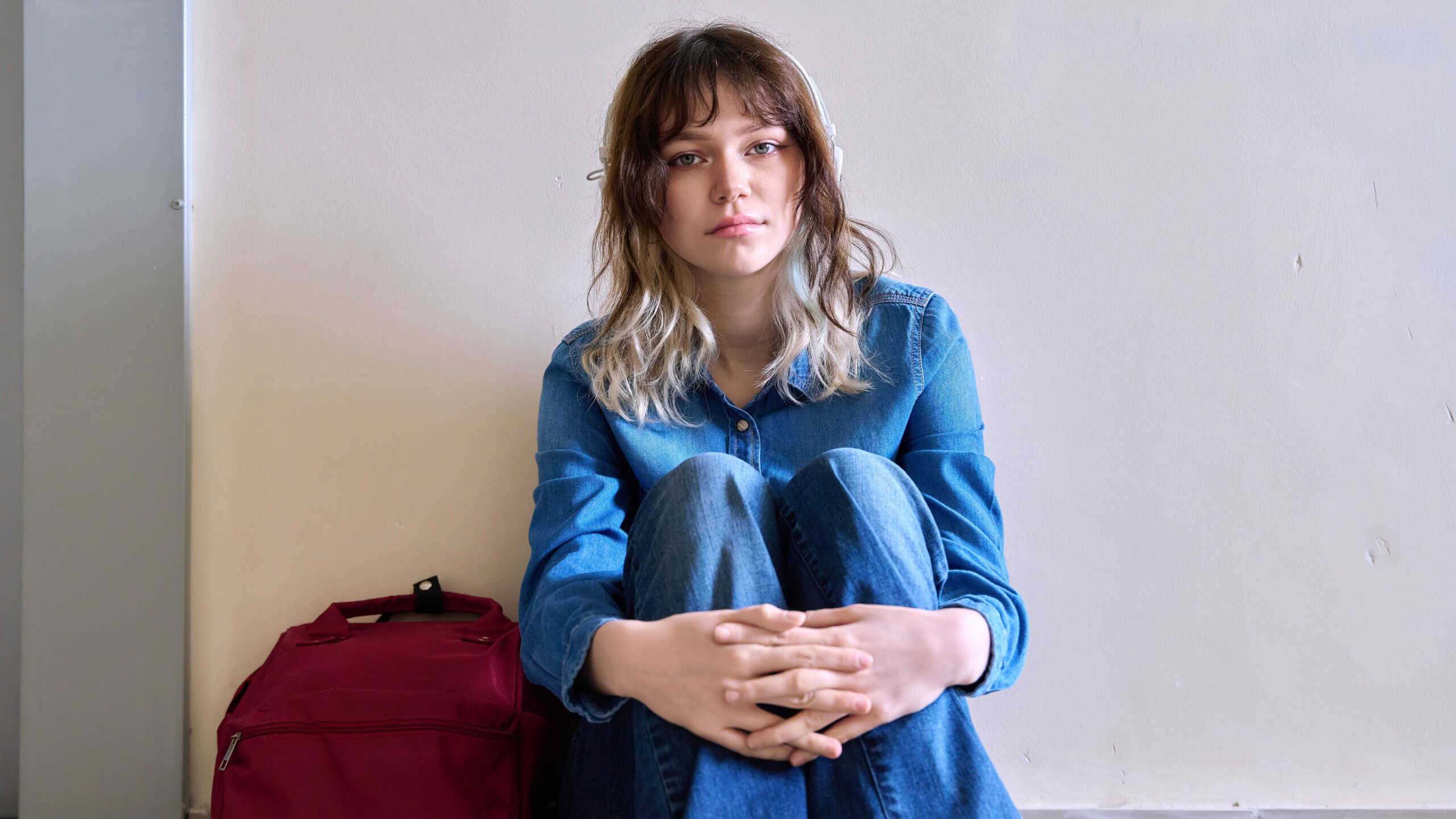 Beautiful teenage female with backpack sitting on floor looking at camera