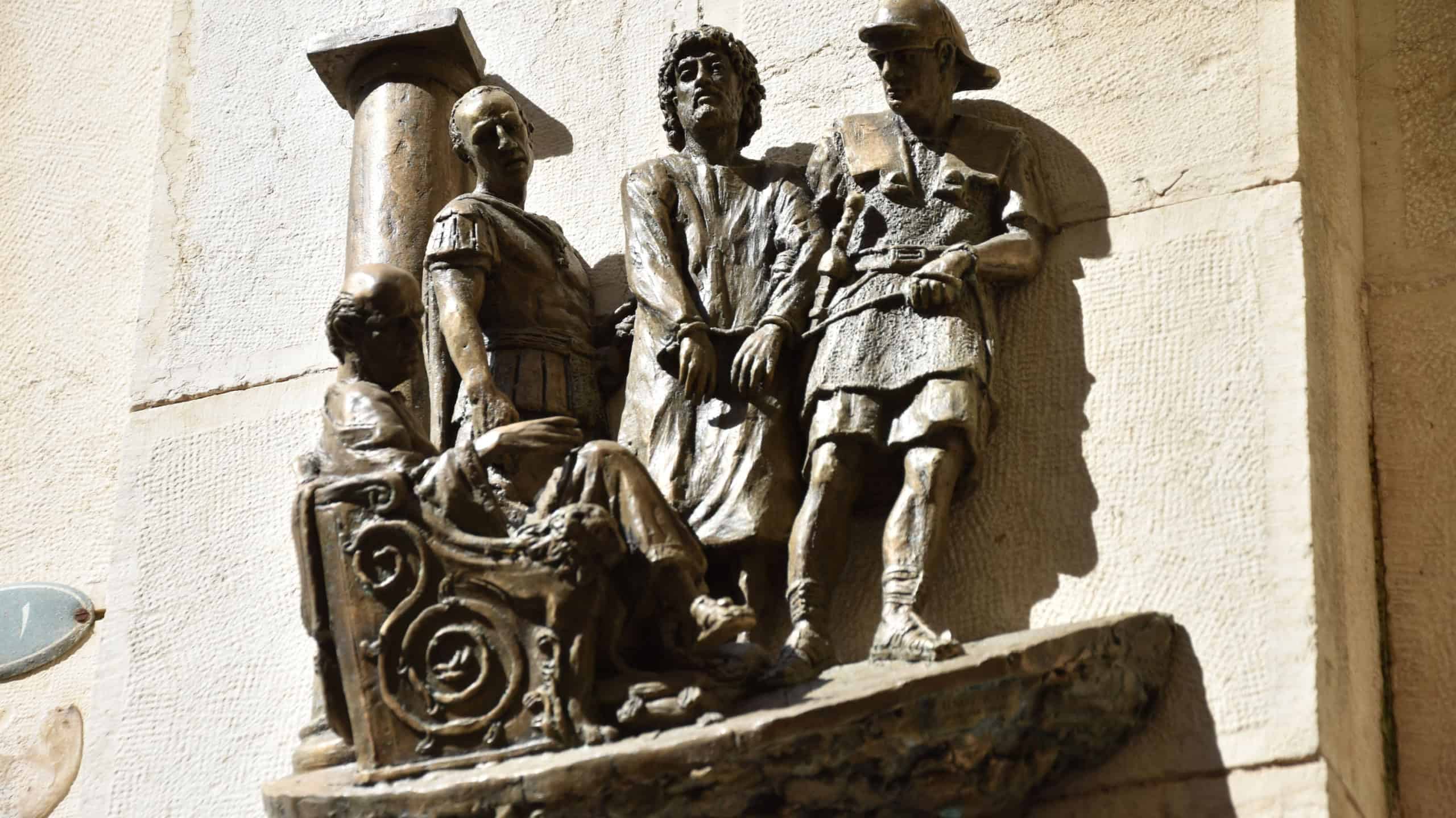 A metal sculpture of Jesus Christ talking to Pontius Pilate on a building's wall