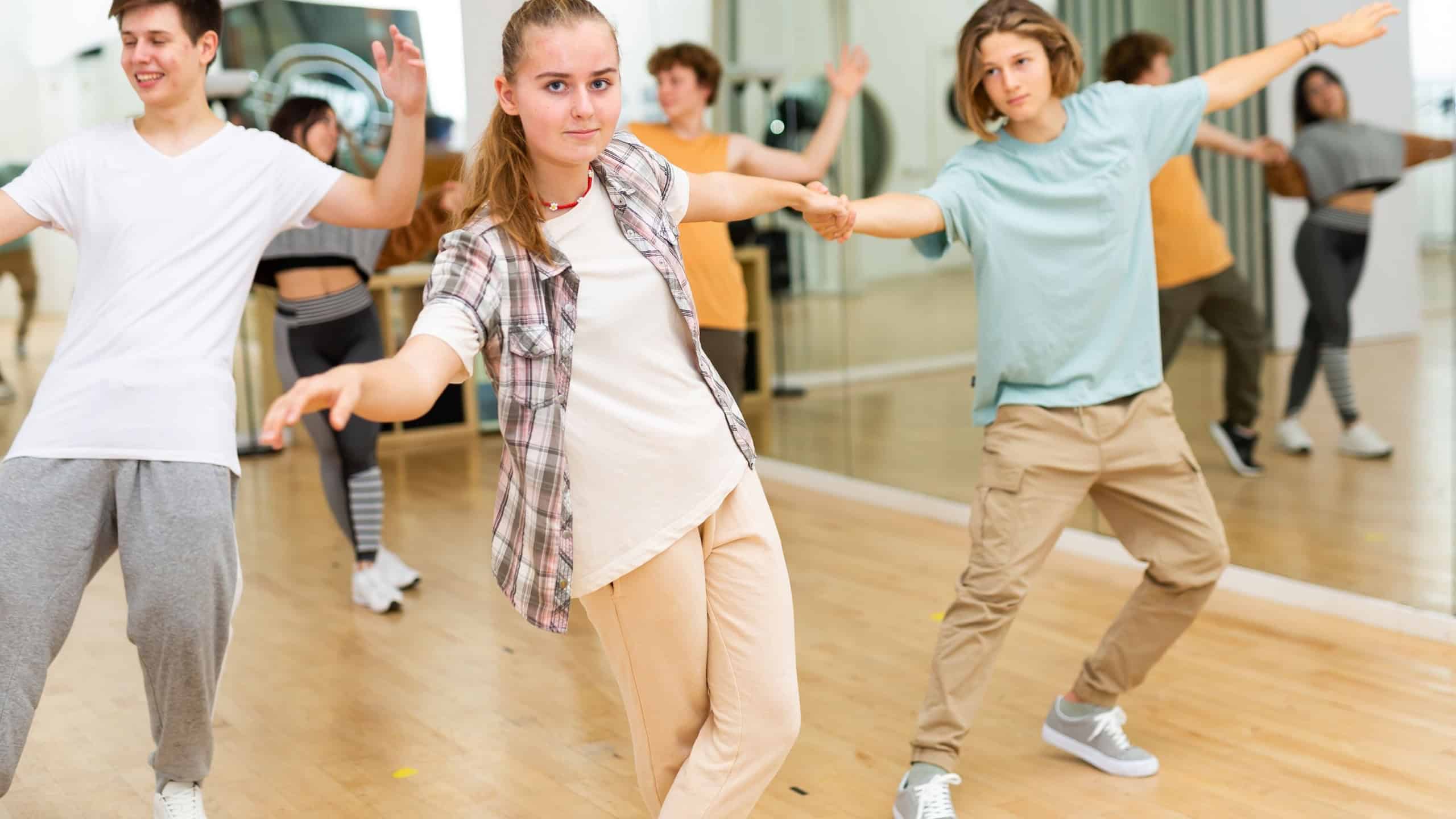 Interested modern teen girl practicing dynamic boogie-woogie in pair with boy during group class in dance studio for youth.