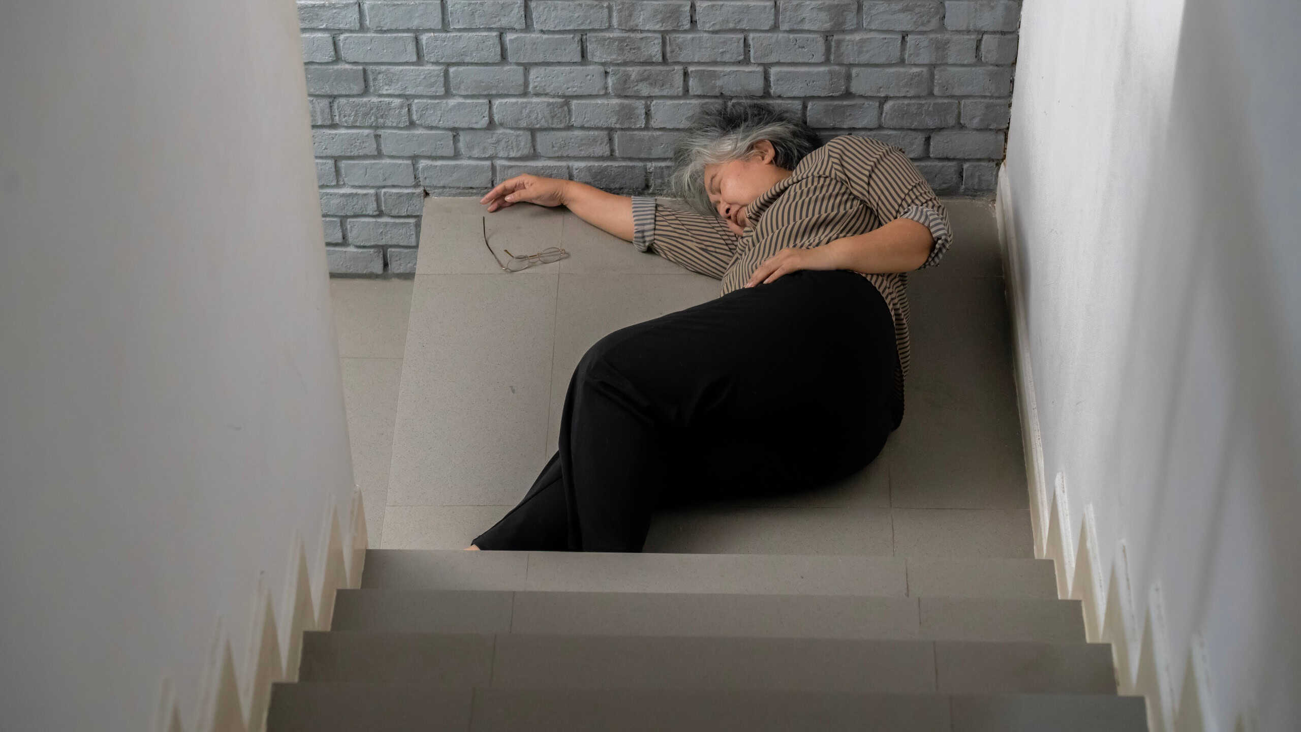 Woman with gray hair is unconscious lying on the floor after an accident falling down the stairs.