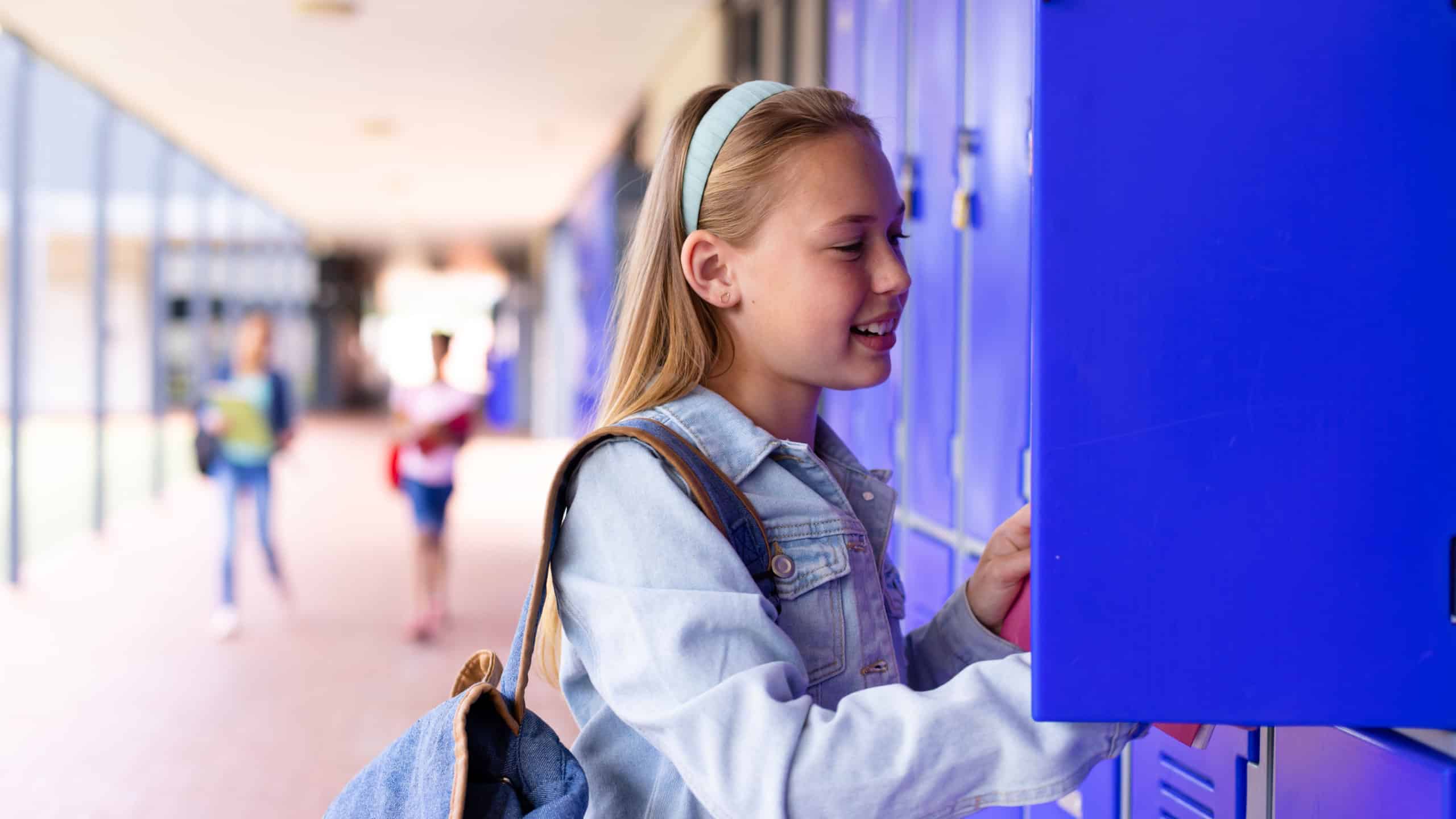 Happy caucasian schoolgirl standing next to lockers in corridor at school. School, education and learning concept.