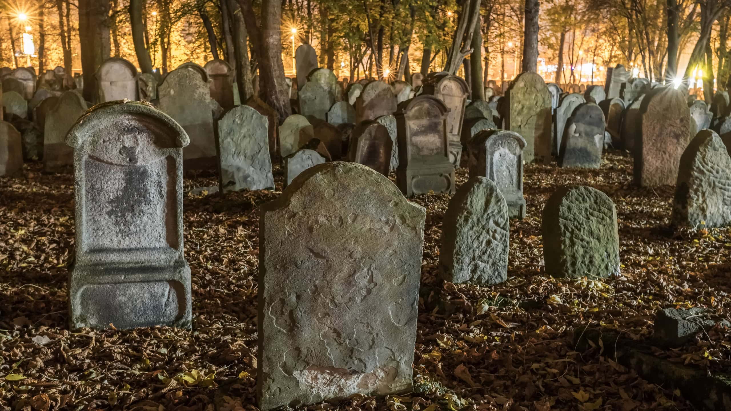 Tombstones in an old cemetery at night in autumn. Blanketed gravestones create a spooky scene. Leaning tombstones add to the eerie ambience. Creepy aged tombstones stand amidst trees in the graveyard.