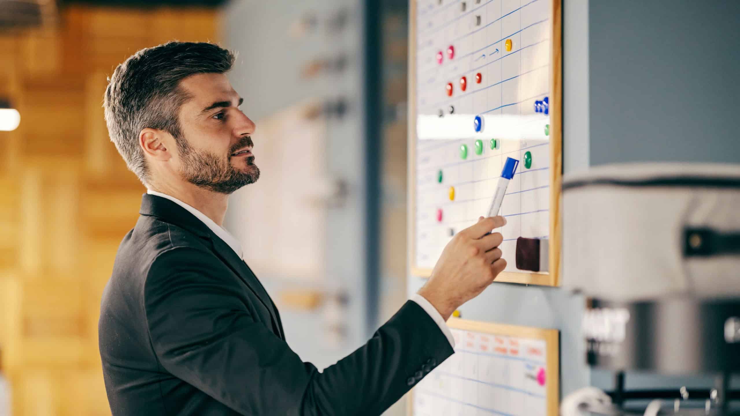 A businessman is looking at planner and planning his next step while standing at workspace.