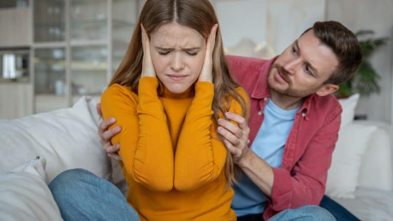 Disappointed woman sitting on sofa, closing ears with hands, doesnt want to hear man justifying, expaining disagreement in relations. Tension, emotional confrontation, misunderstanding in family life