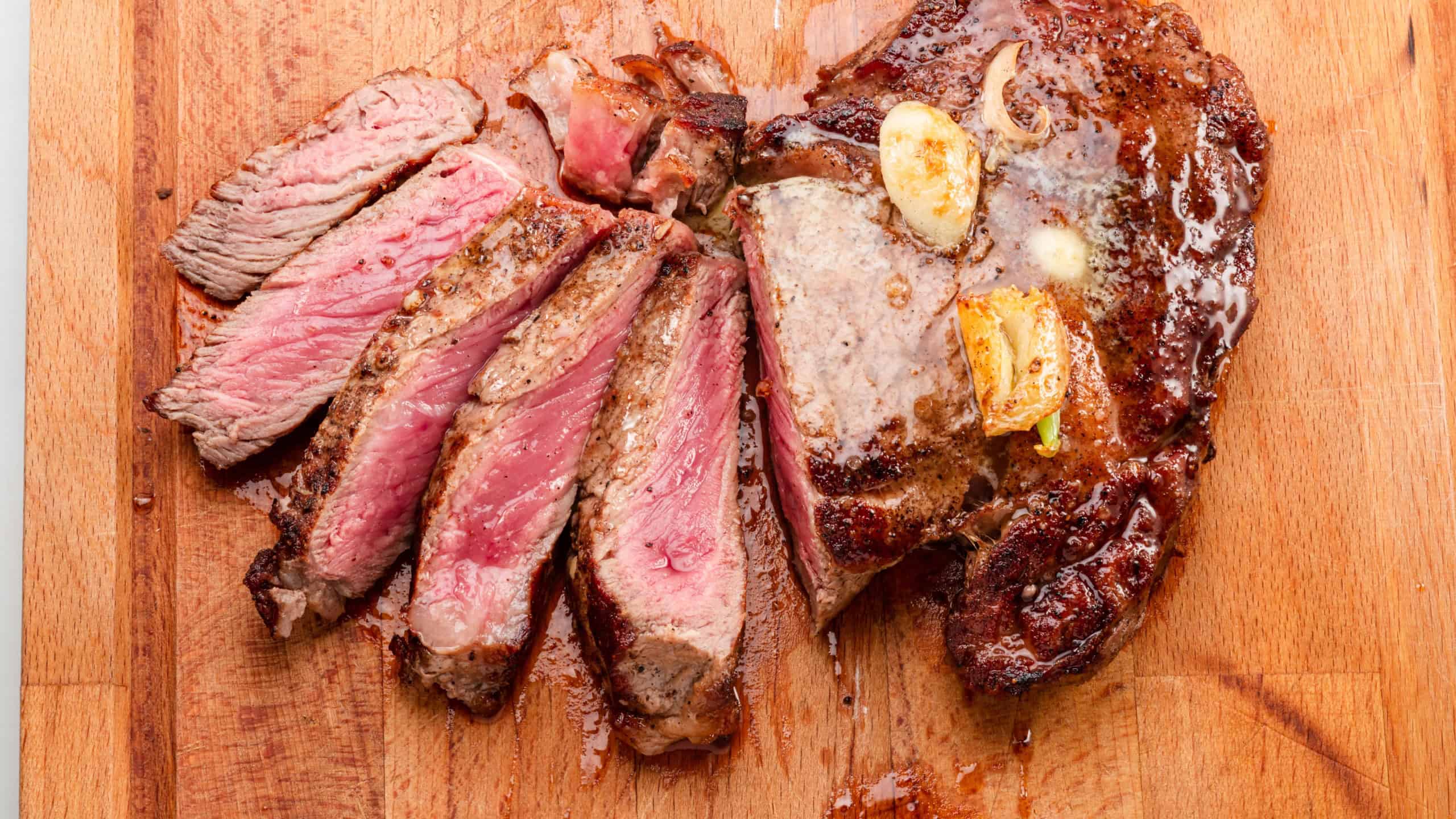 Sliced juicy medium rib eye steak on wooden board. Top view.