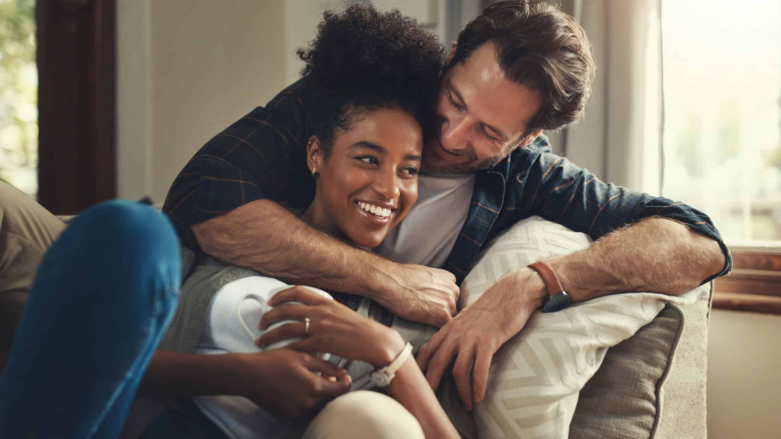 Home, happy and couple with hug on sofa for weekend romance, partnership and bonding together. Man, love and woman with affection in living room on couch for connection, support and trust in marriage
