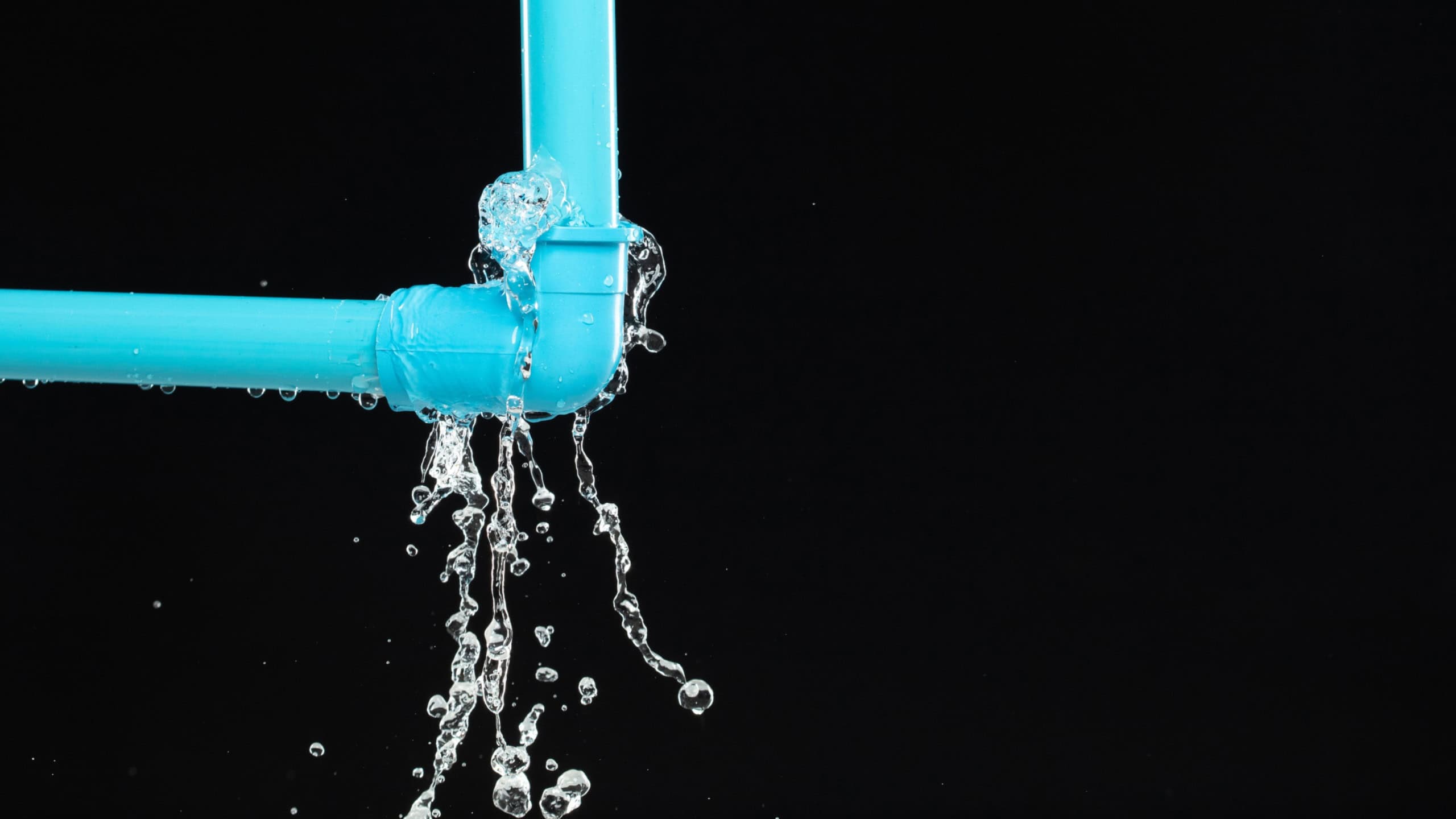 Leaking water from blue pvc plastic pipe under sink. Drain leak water from blue pvc plastic pipe broken connection plumbing in bathroom. Black background isolated