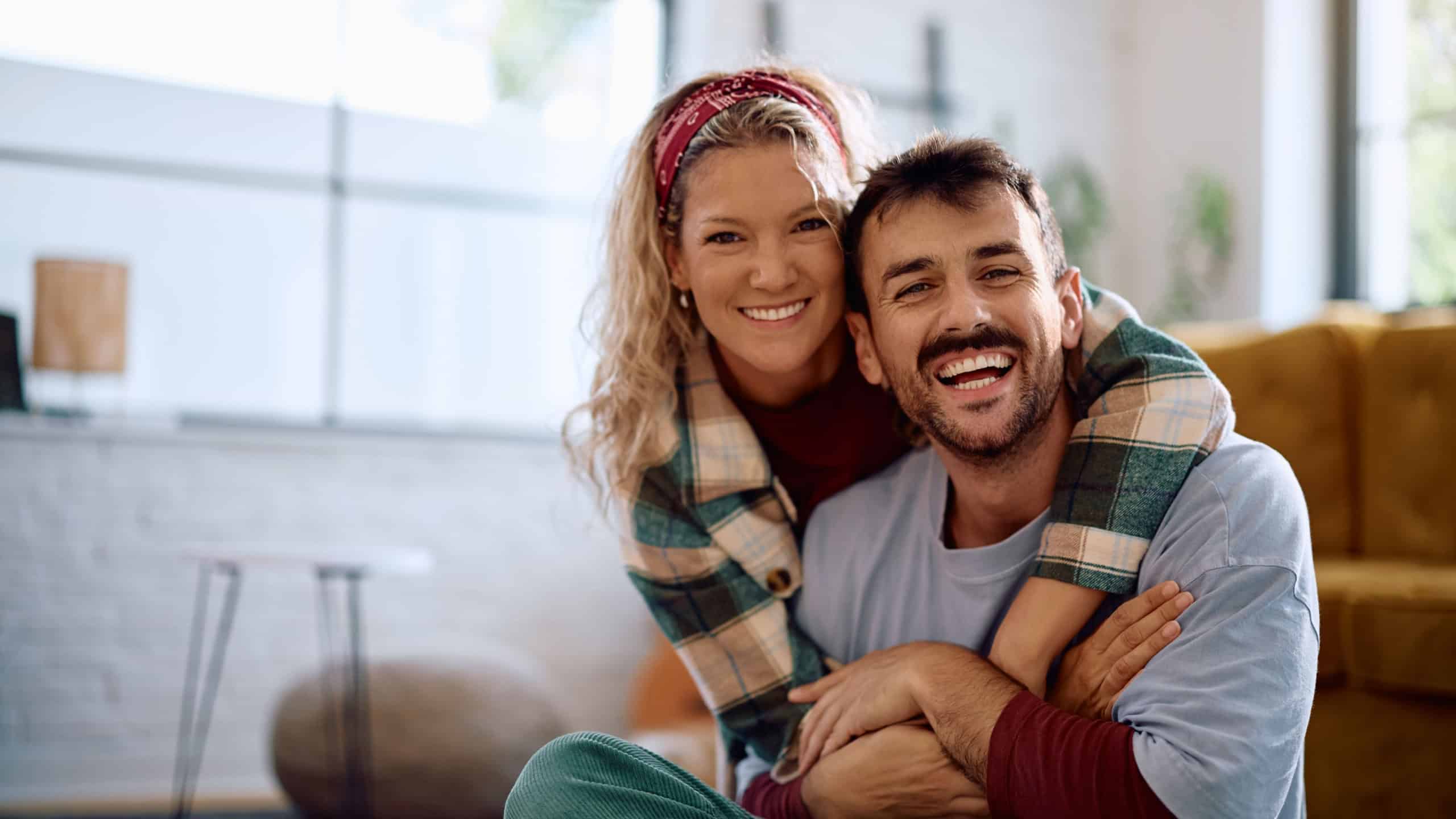 Happy embraced couple relaxing at home and looking at camera. Copy space.