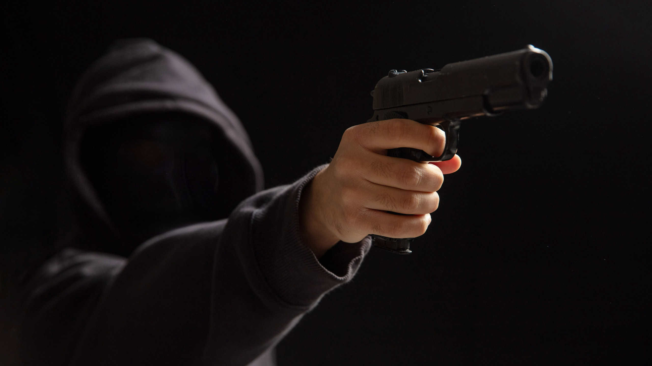 Robber wearing black hood holding gun, ready to shoot. Armed gangster criminal, killer. Weapon, violence concept