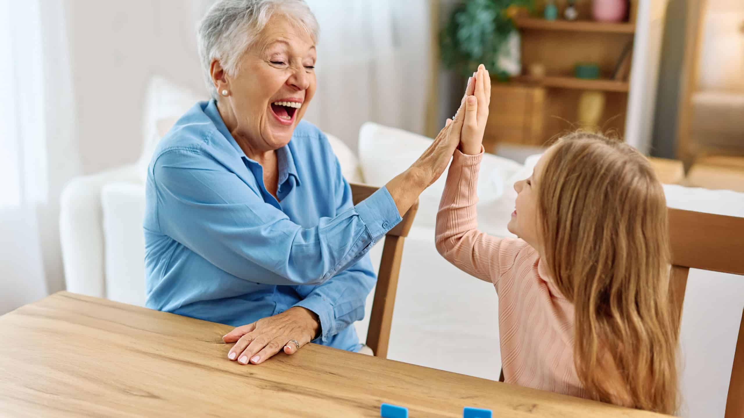 Portrait of grandmother and granddaughter having fun together playing a board game domino game at home
