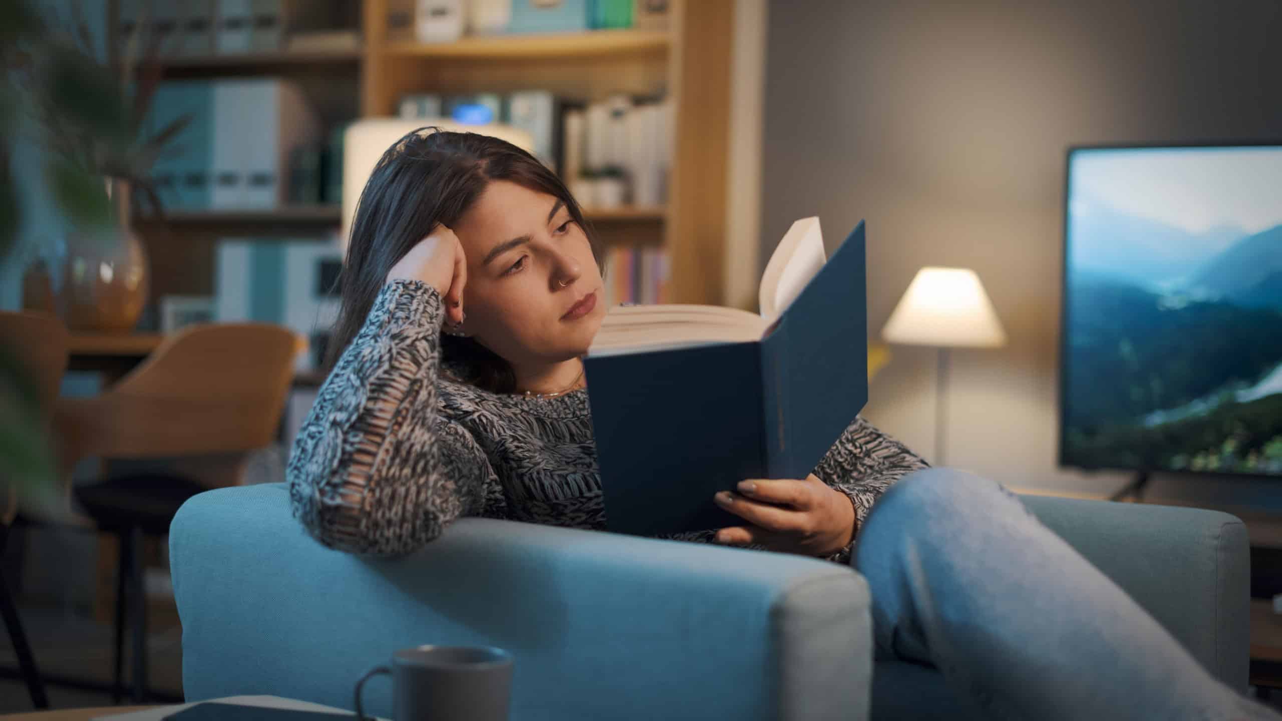 Relaxed happy woman resting on the armchair at home in the living room and reading a book