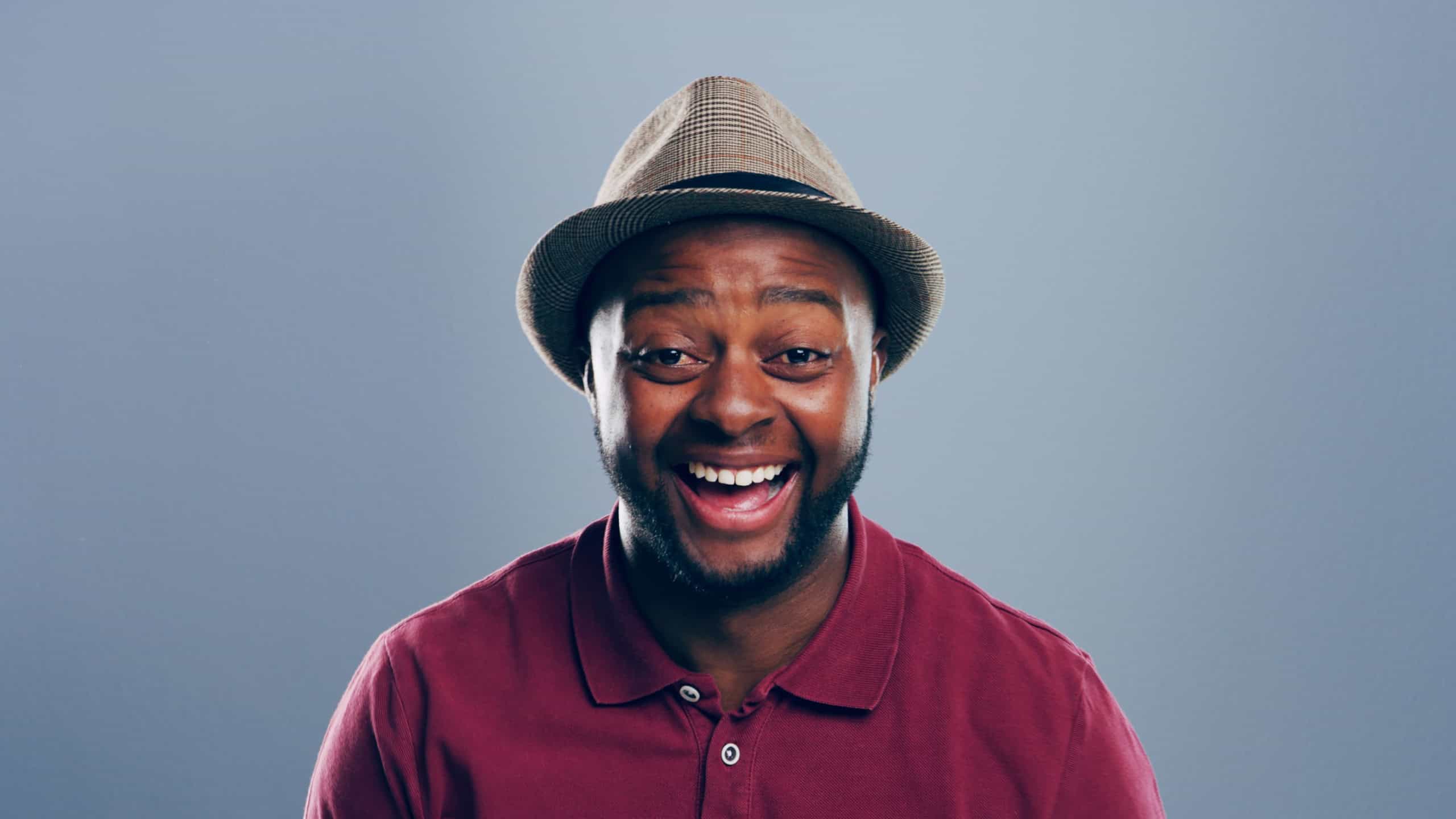 Portrait, black man and laughing in studio for funny joke, comedy and happy with space. Face, smile and African person with humor, excited and LOL with comic emotion on gray background with hat