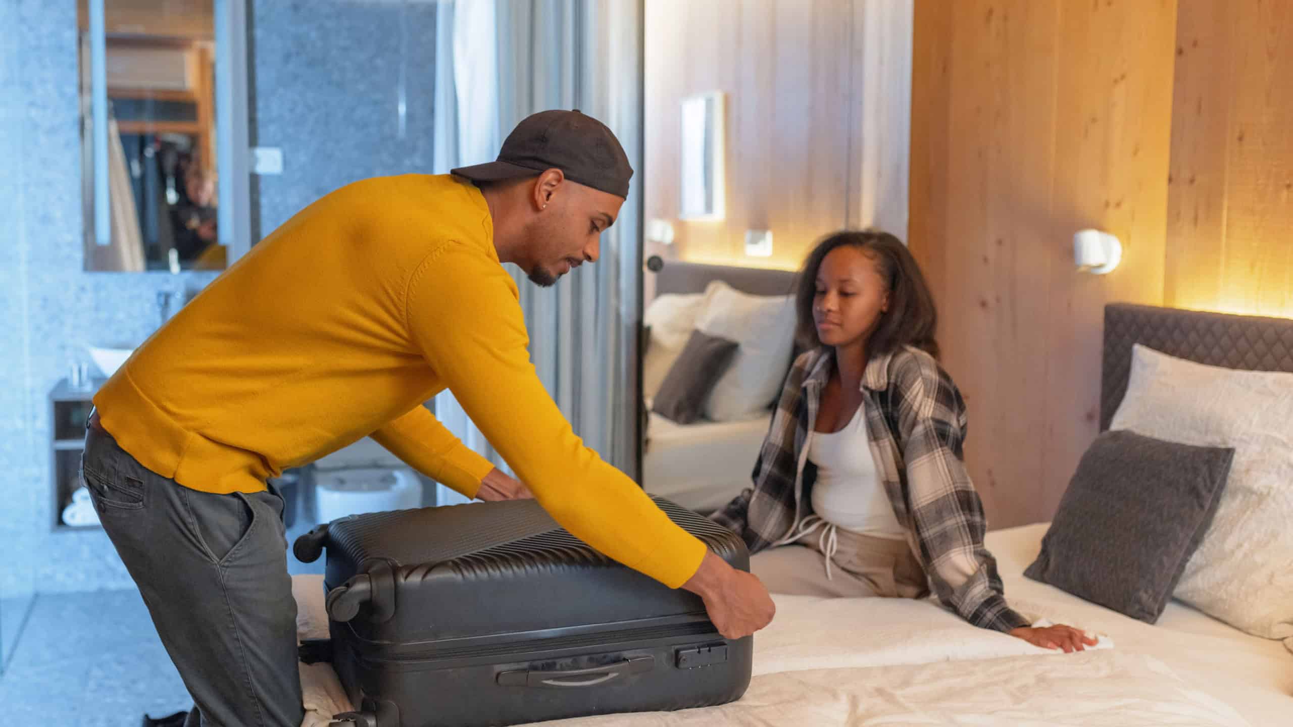 African American couple chatting while packing a suitcase in a hotel room on the last day of vacation. Travel lifestyles concept.