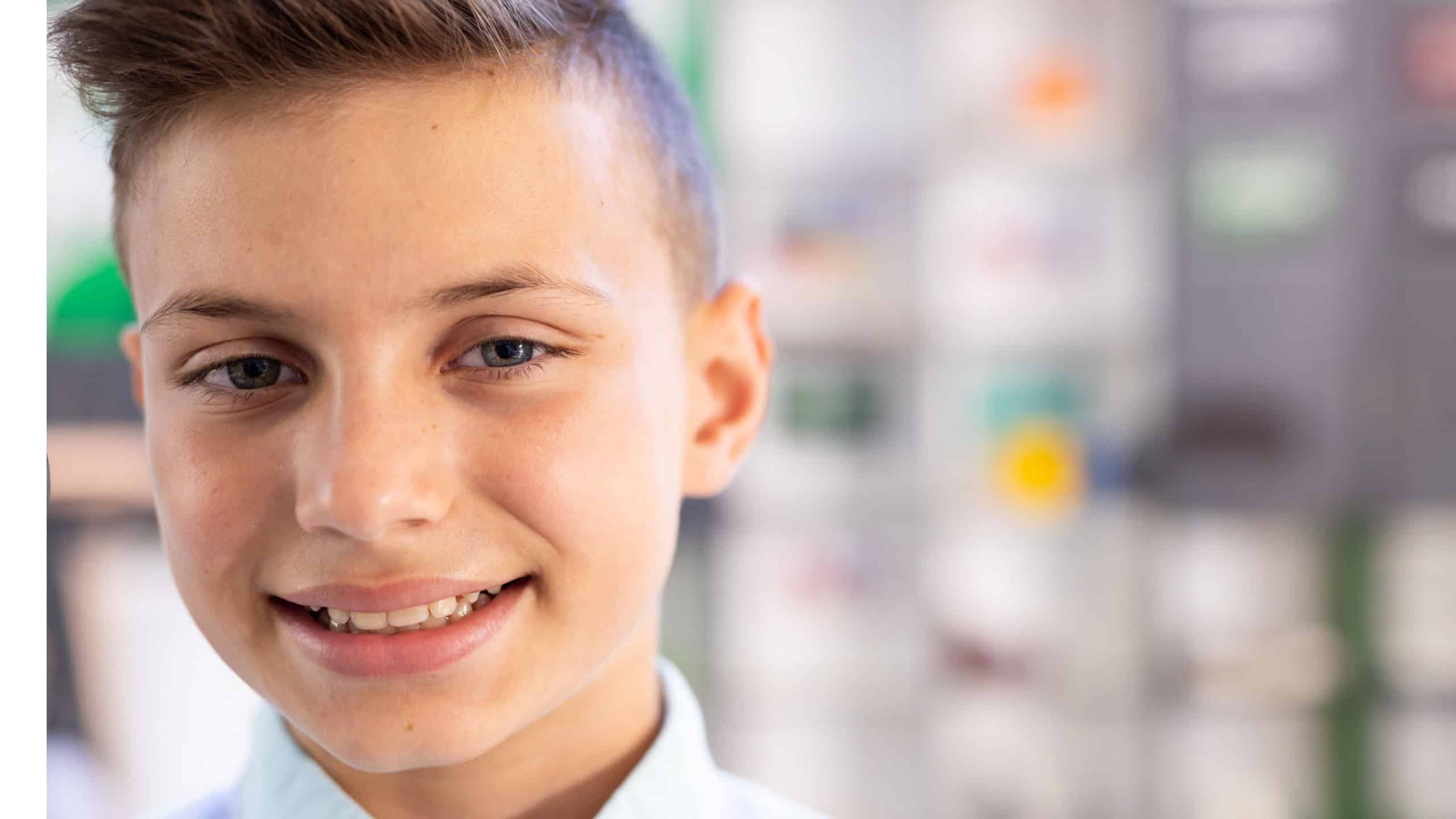 Boy child smiling and looking at camera in school classroom, with grid of colorful pictures behind. Portrait, headshot, casual, vibrant, bokeh, collared, academic