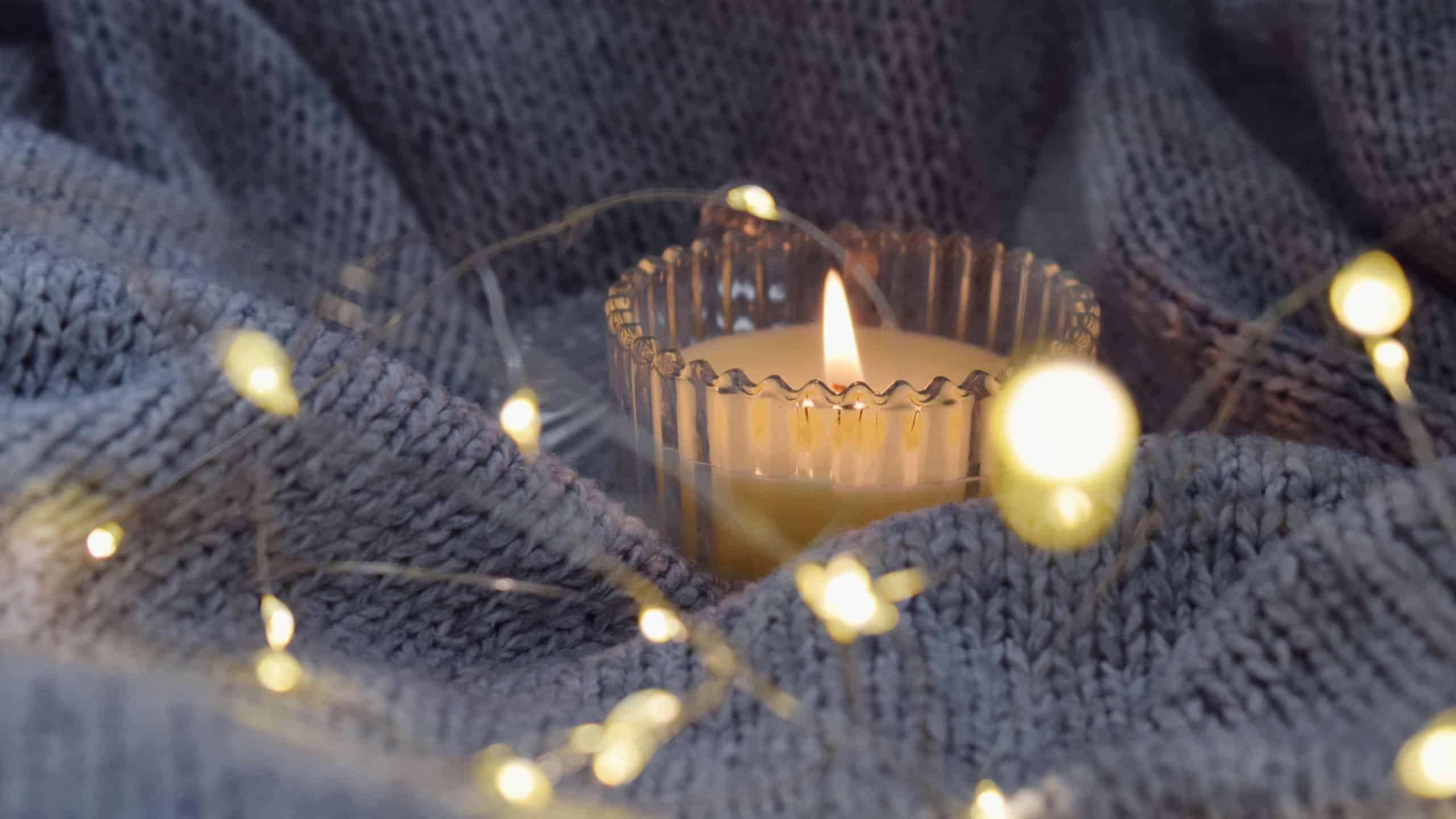 Knitted grey blanket in soft garland lighting. Cozy atmosphere with candle.