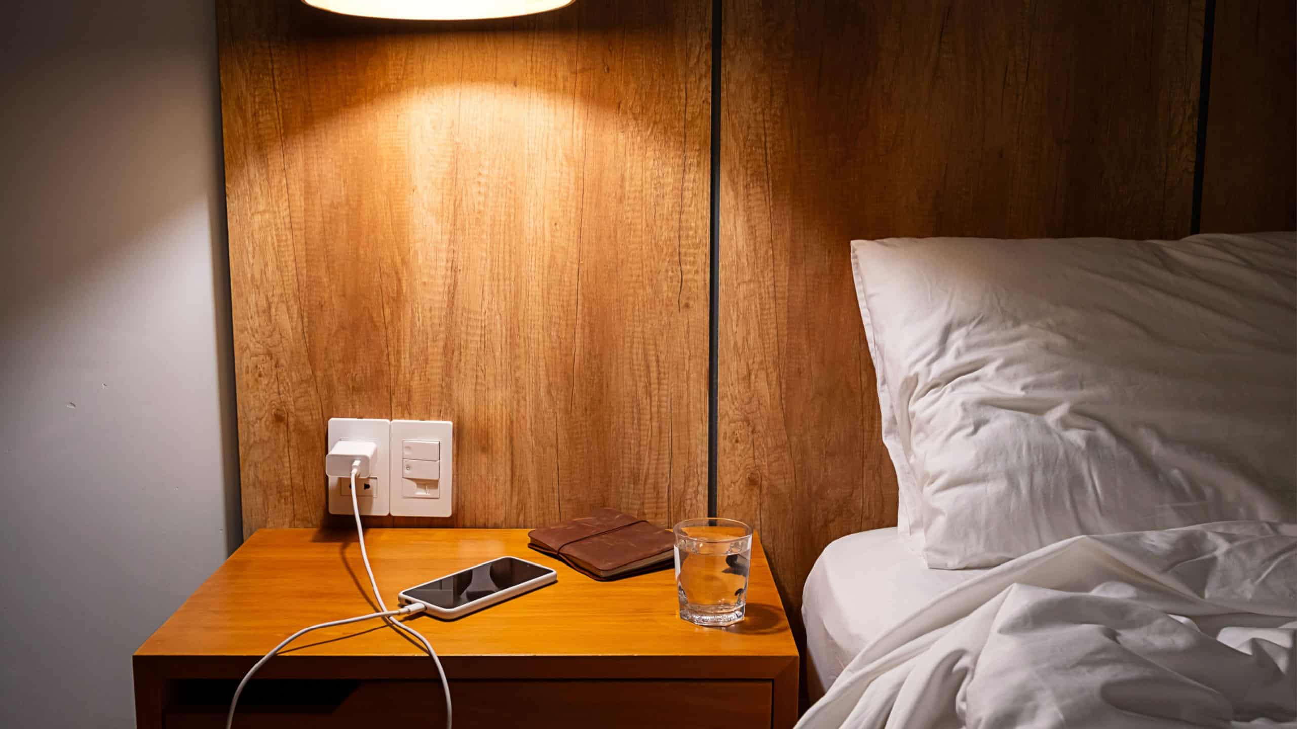 Mobile phone charging on bedside table in comfortable hotel or home bedroom. Modern living and relaxation.