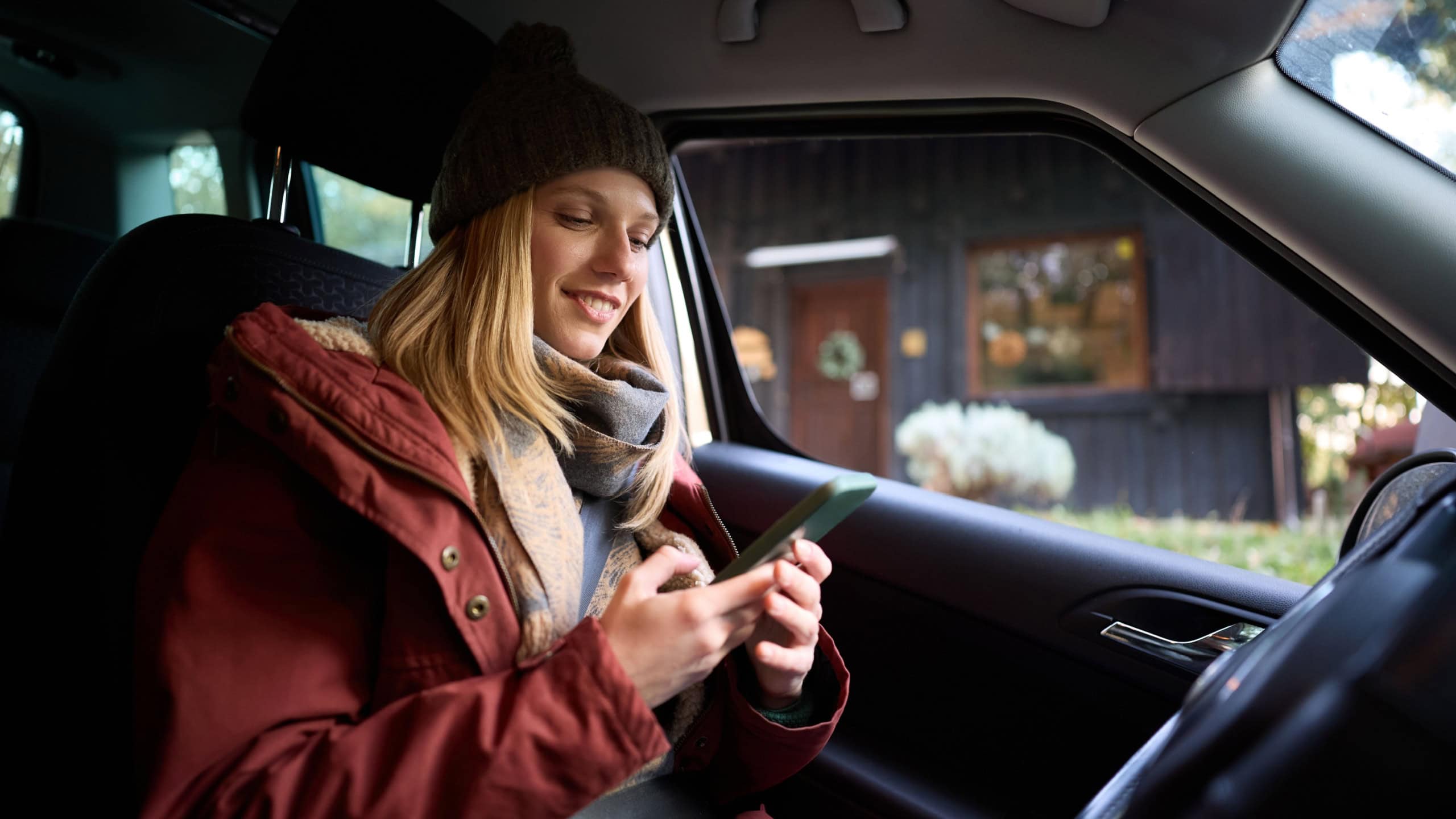 Happy woman using app on smart phone while sitting in a car.