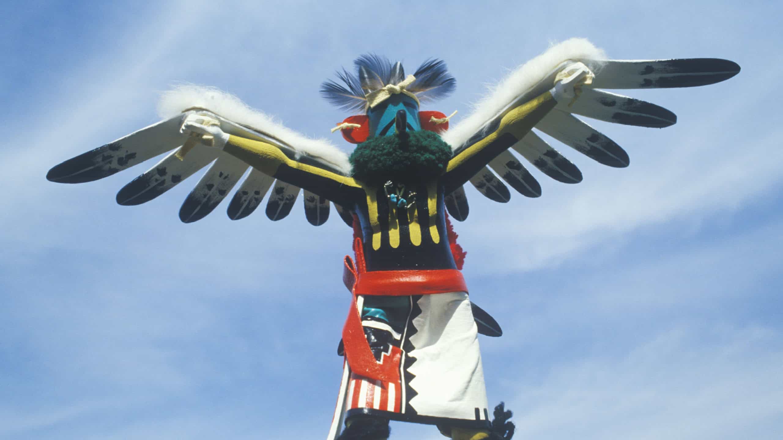 Hopi Kachina doll with outstretched winged arms against blue sky