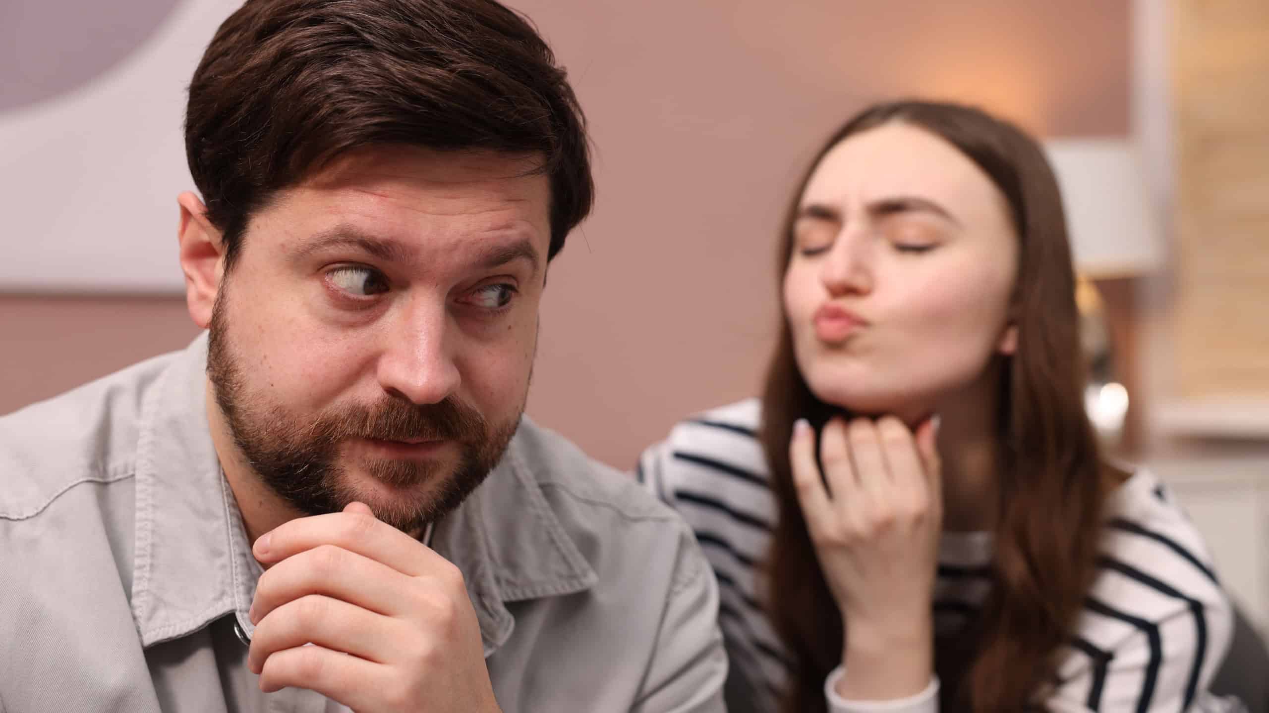 Embarrassed man refusing kiss from young woman at home, selective focus