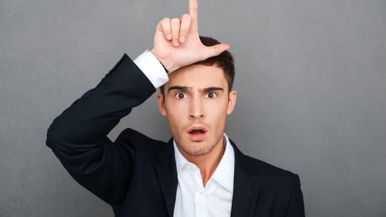Loser! Frustrated young man in formalwear gesturing loser sign and looking at camera
