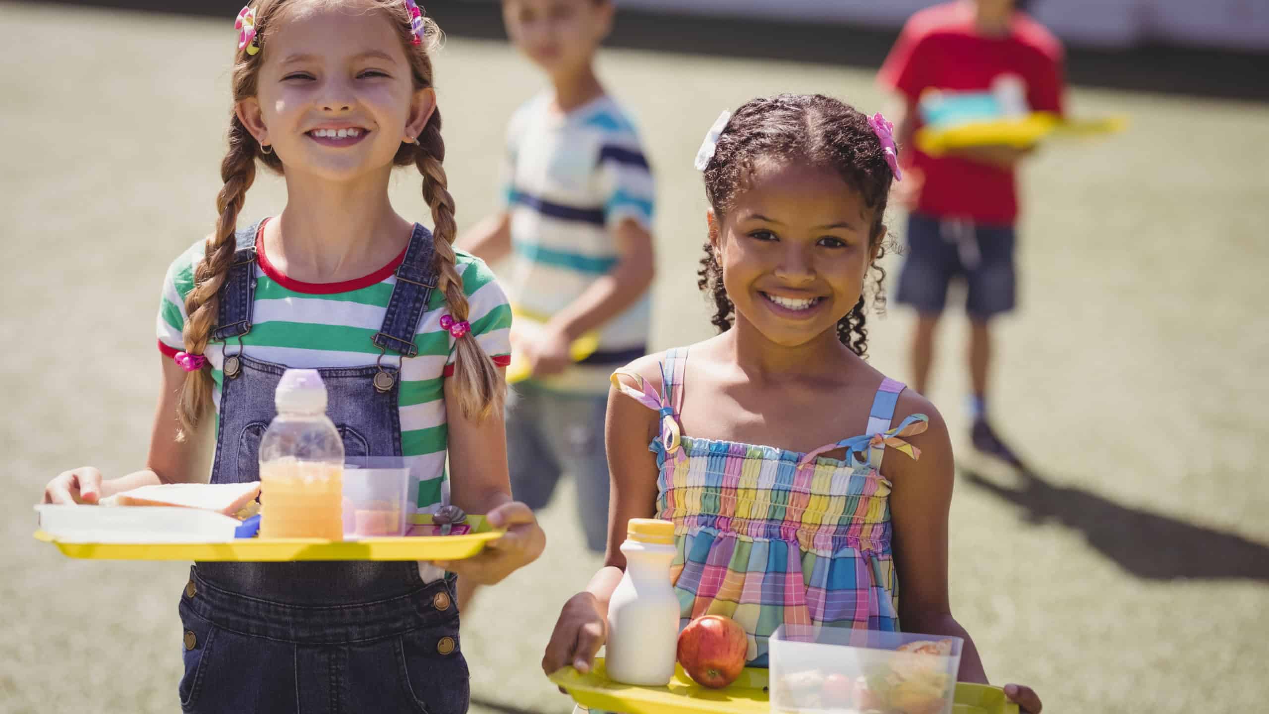 Portrait of happy schoolgirls holding meal in tray at school