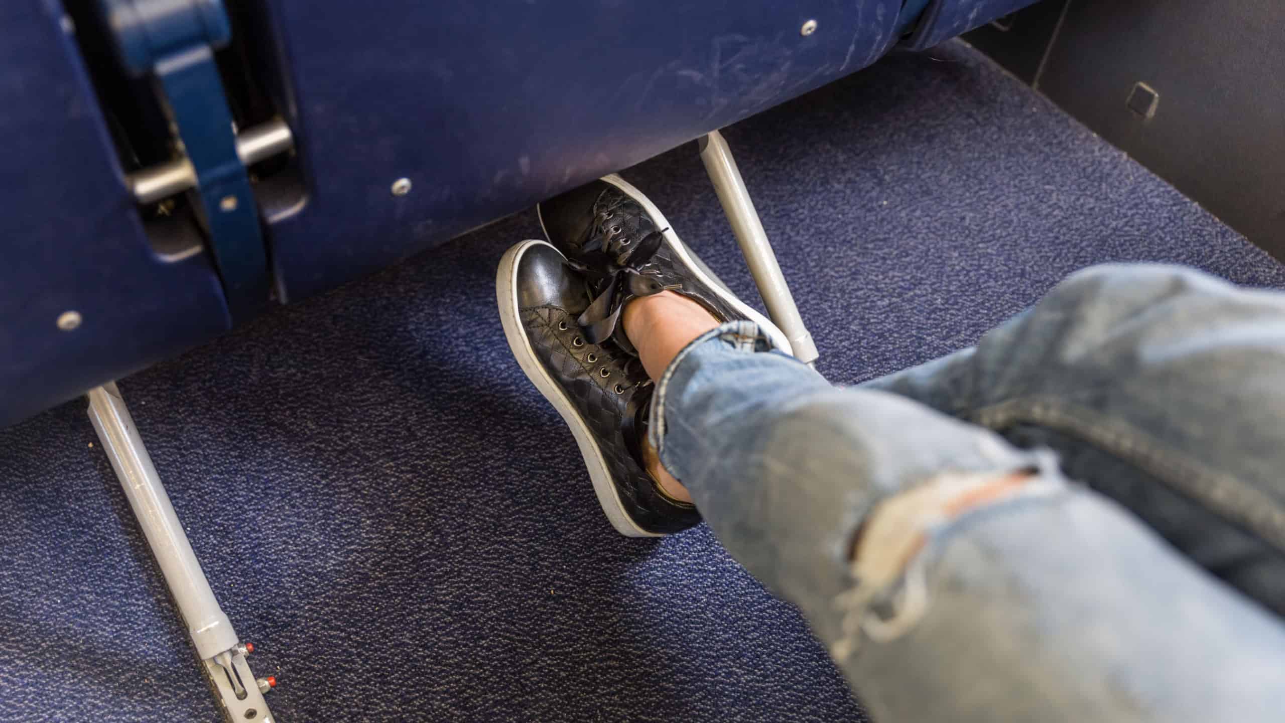 Female passenger stretching her legs on long commercial airplane flight. Exit seats with more leg space for more comfortable flight.