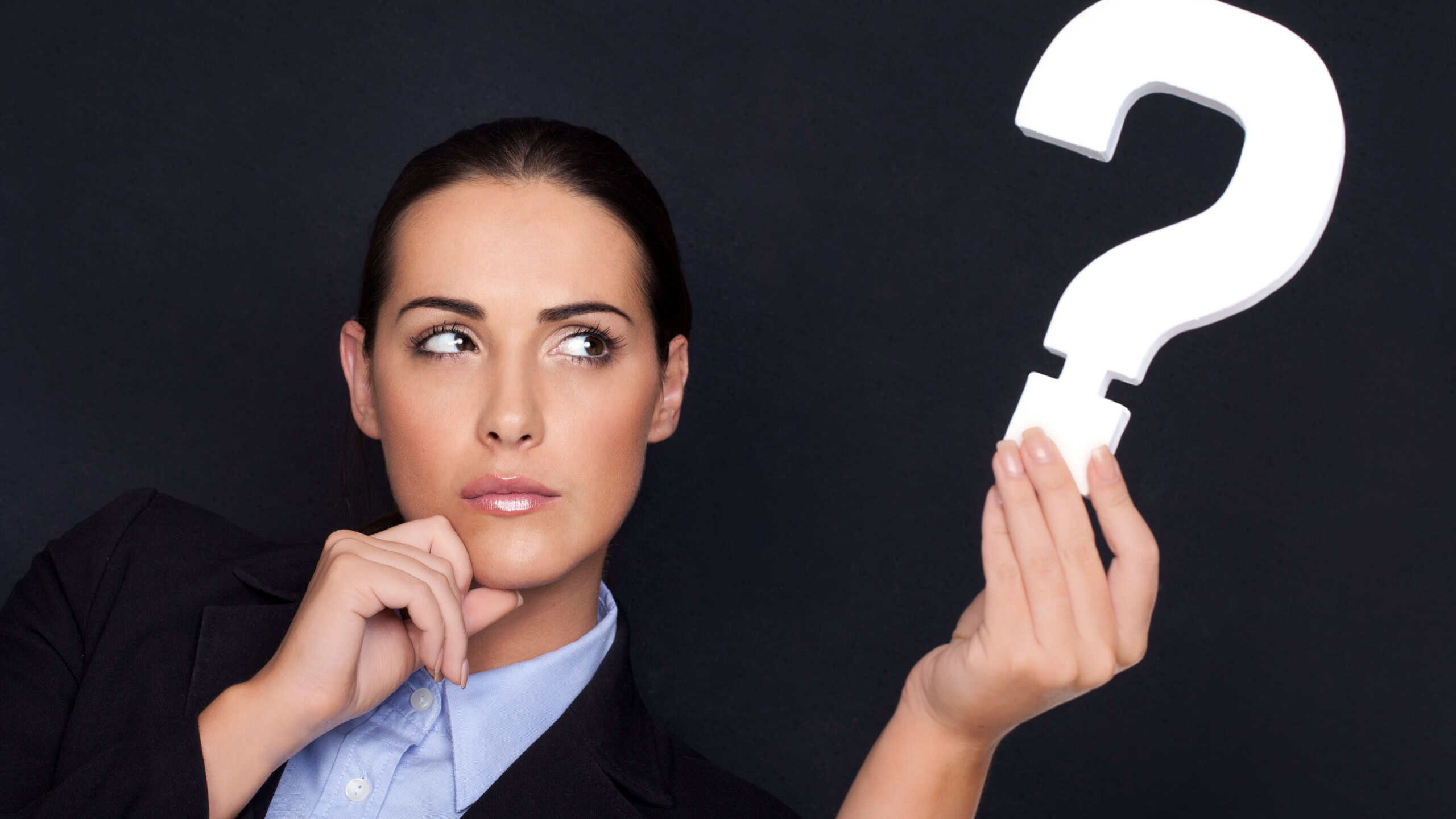 Beautiful businesswoman with a thoughtful expression holding a white question mark in her hand against a black studio background