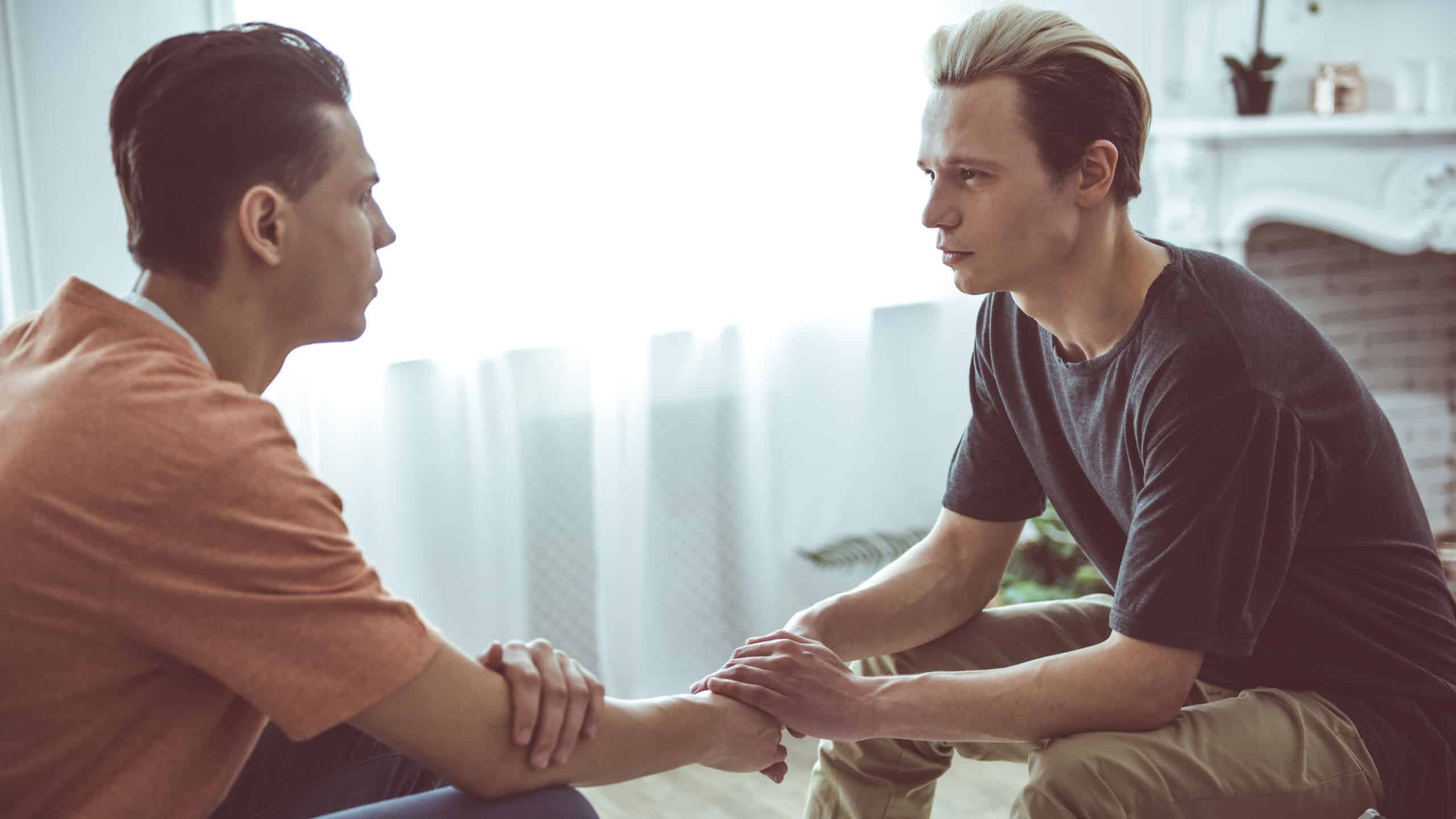 Side view portrait of two handsome guys sitting on couch and looking at each other while sharing tender moment