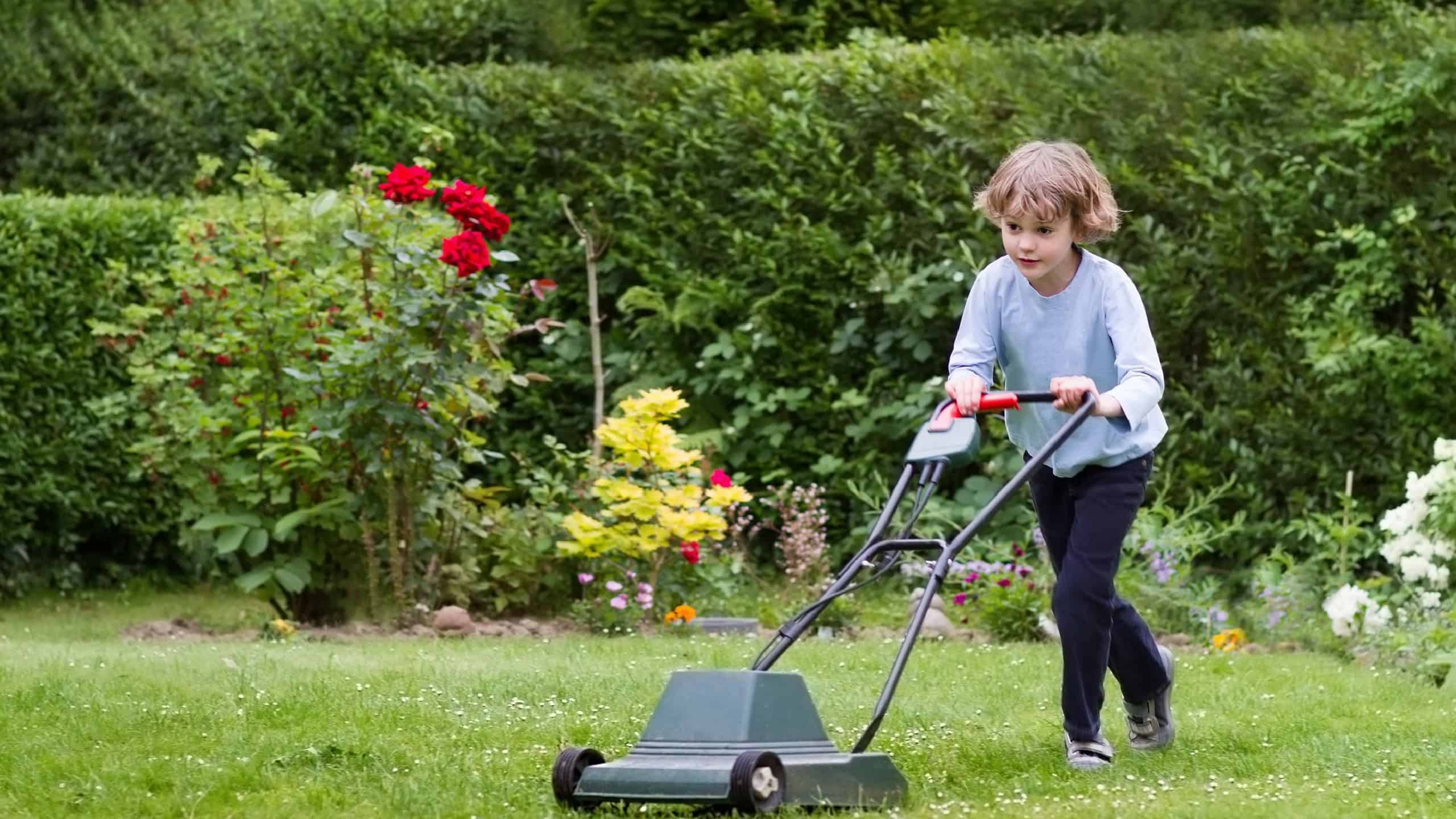 Little boy playing with a lawn mower in the garden