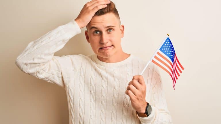 Young handsome man holding USA flag over isolated white background stressed with hand on head, shocked with shame and surprise face, angry and frustrated. Fear and upset for mistake.