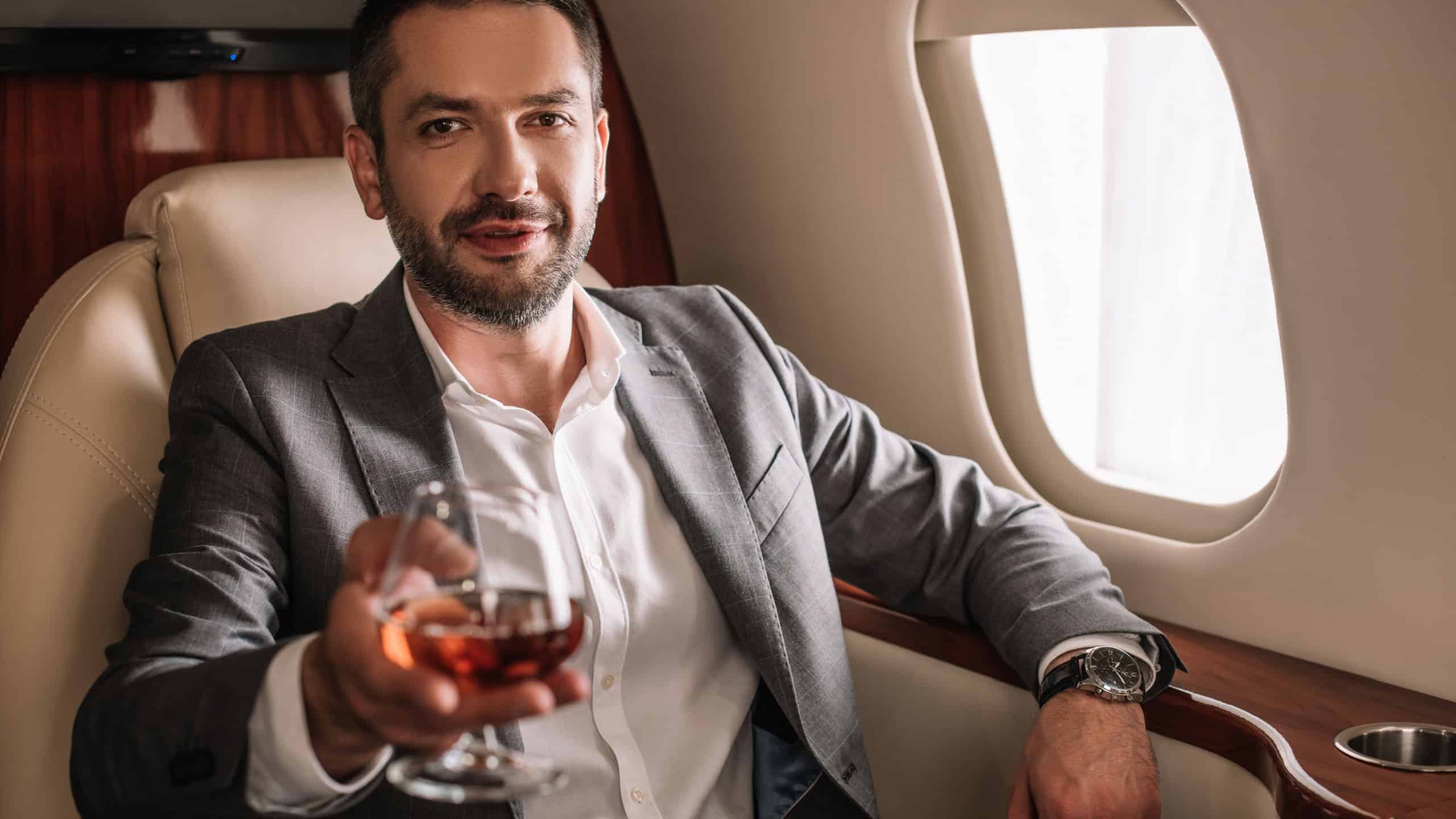selective focus of handsome businessman holding glass with cognac in private jet