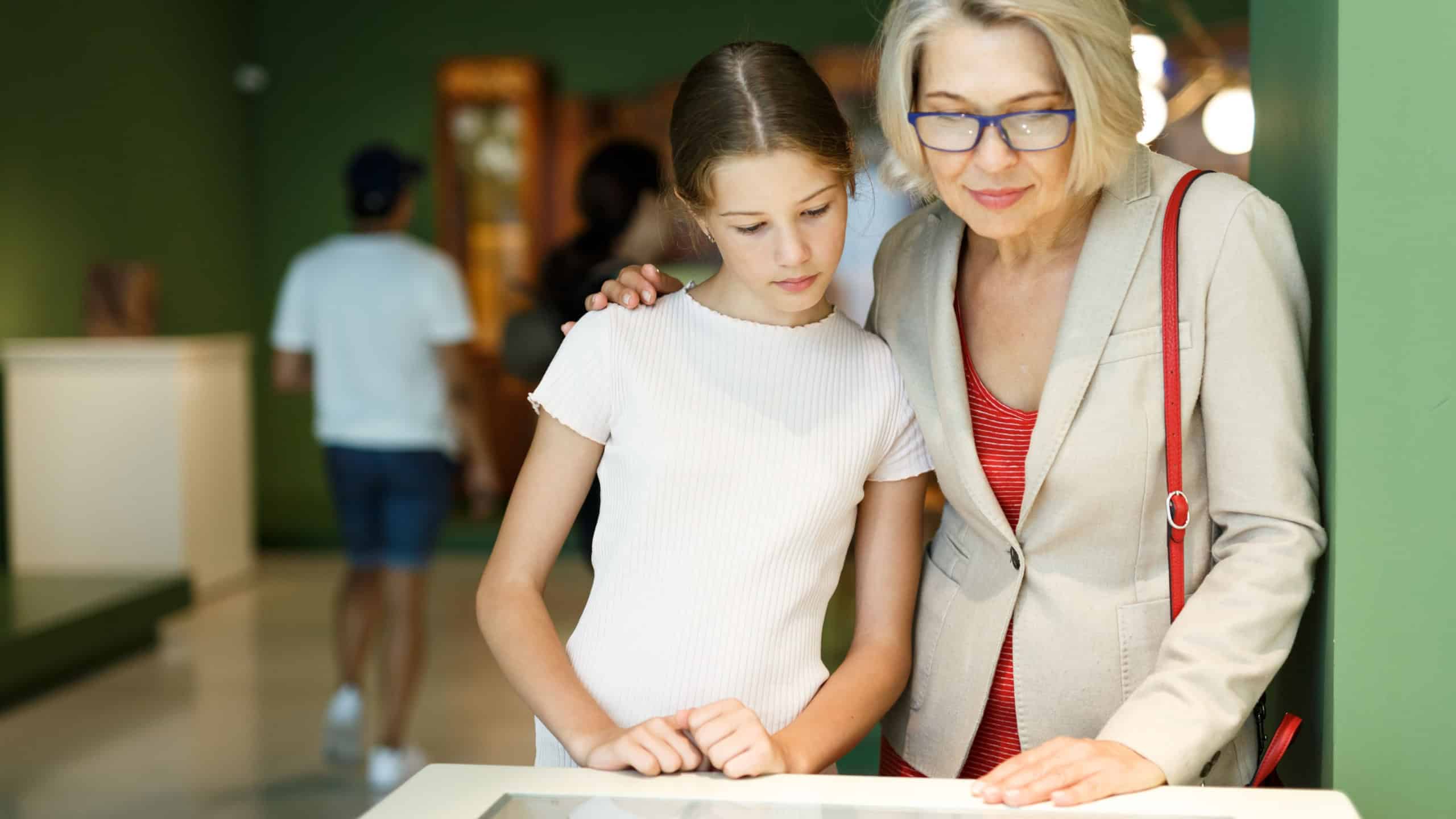 Teenage girl and mature woman observing exhibition in historical museum