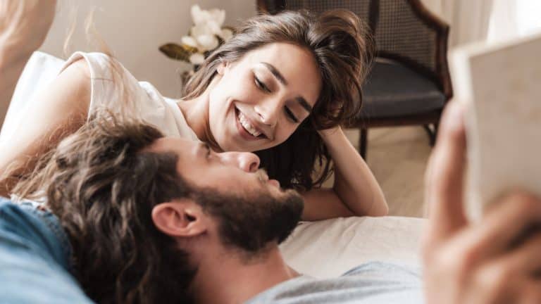 Image of a positive amazing young loving couple indoors at home lies reading book together.