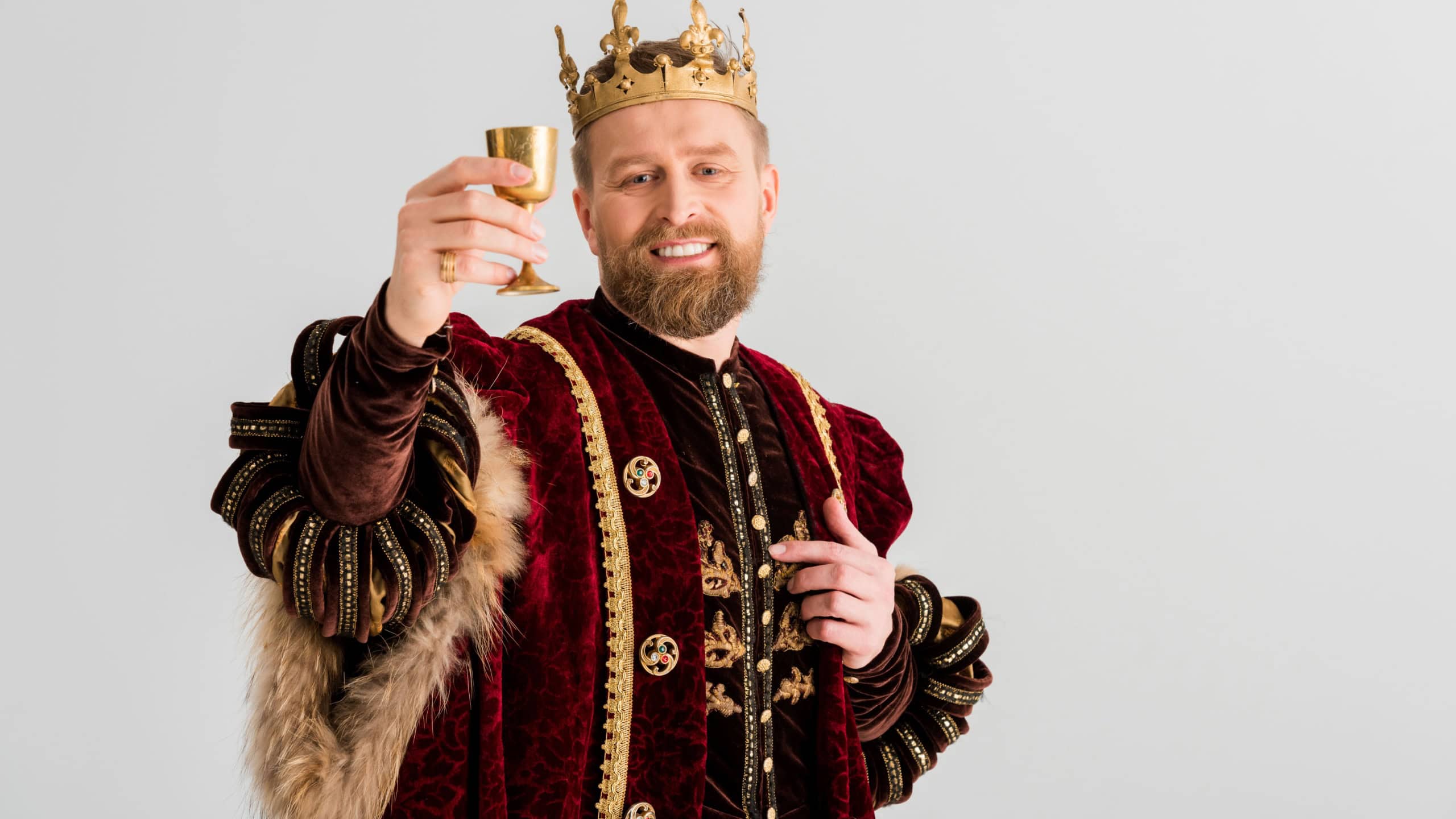 Smiling king with crown holding cup isolated on grey