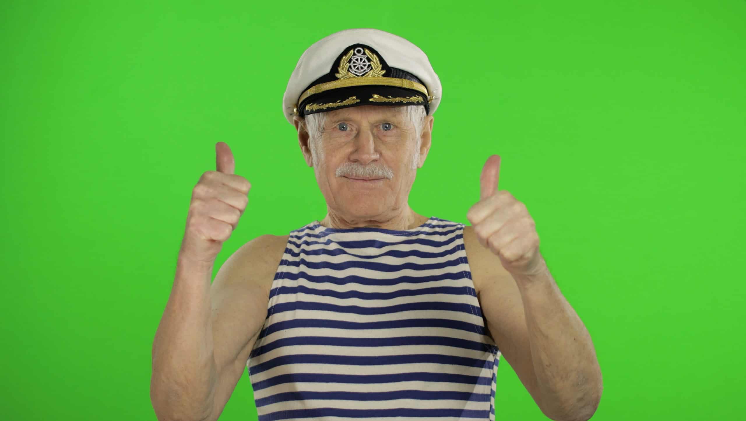 Elderly sailor man show OK sign. Thumbs up. Old man with mustache in hat and striped shirt on chroma key background. Place for your logo or text. Green screen background