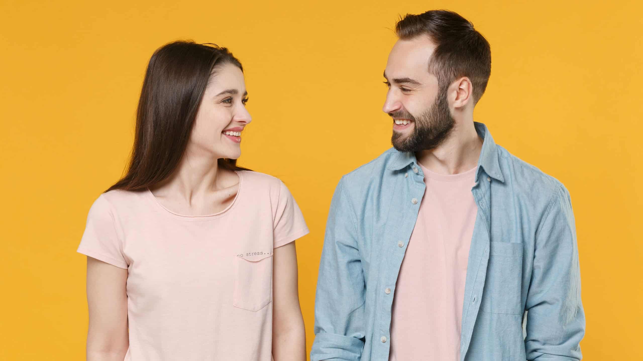 Smiling young couple two friends guy girl in pastel blue casual clothes posing isolated on yellow wall background studio portrait. People lifestyle concept. Mock up copy space. Looking at each other