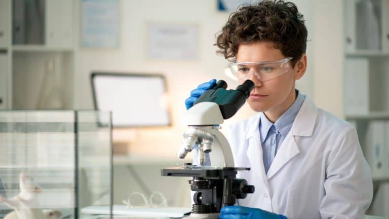 Contemporary young female researcher looking at antibodies in microscope while making experiment with mice in laboratory