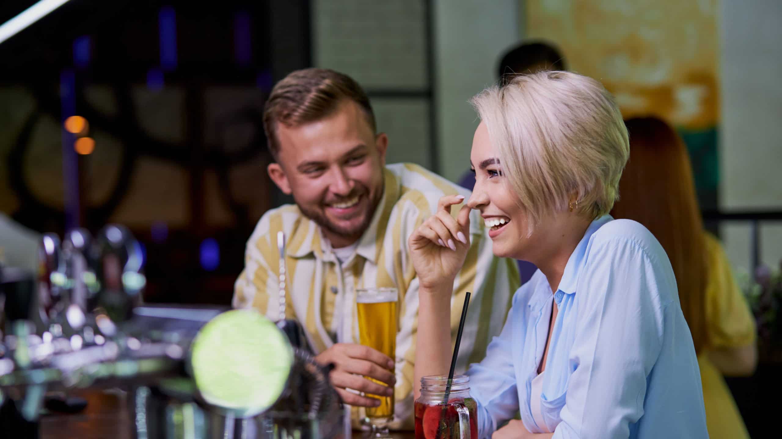 The girl likes the jokes of a stranger, caucasian guy flirt with blond girl in a pub or bar