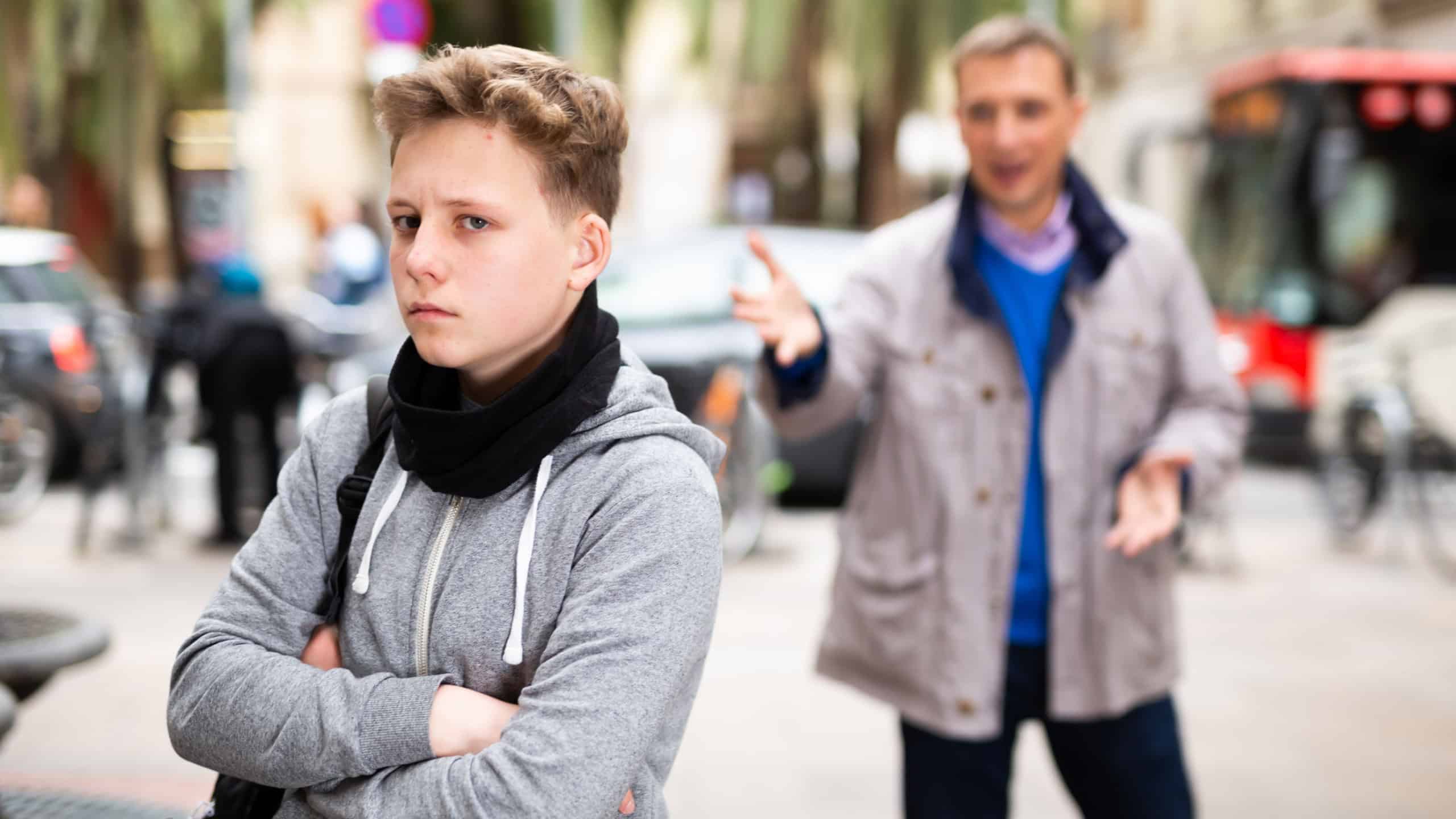 Portrait of upset teenage boy scolded by father outdoors in autumn day. Family conflicts concept